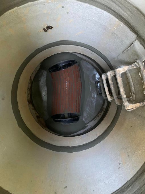 Close-up of a metal cylindrical chamber with a dark circular opening and a small latch on the right.