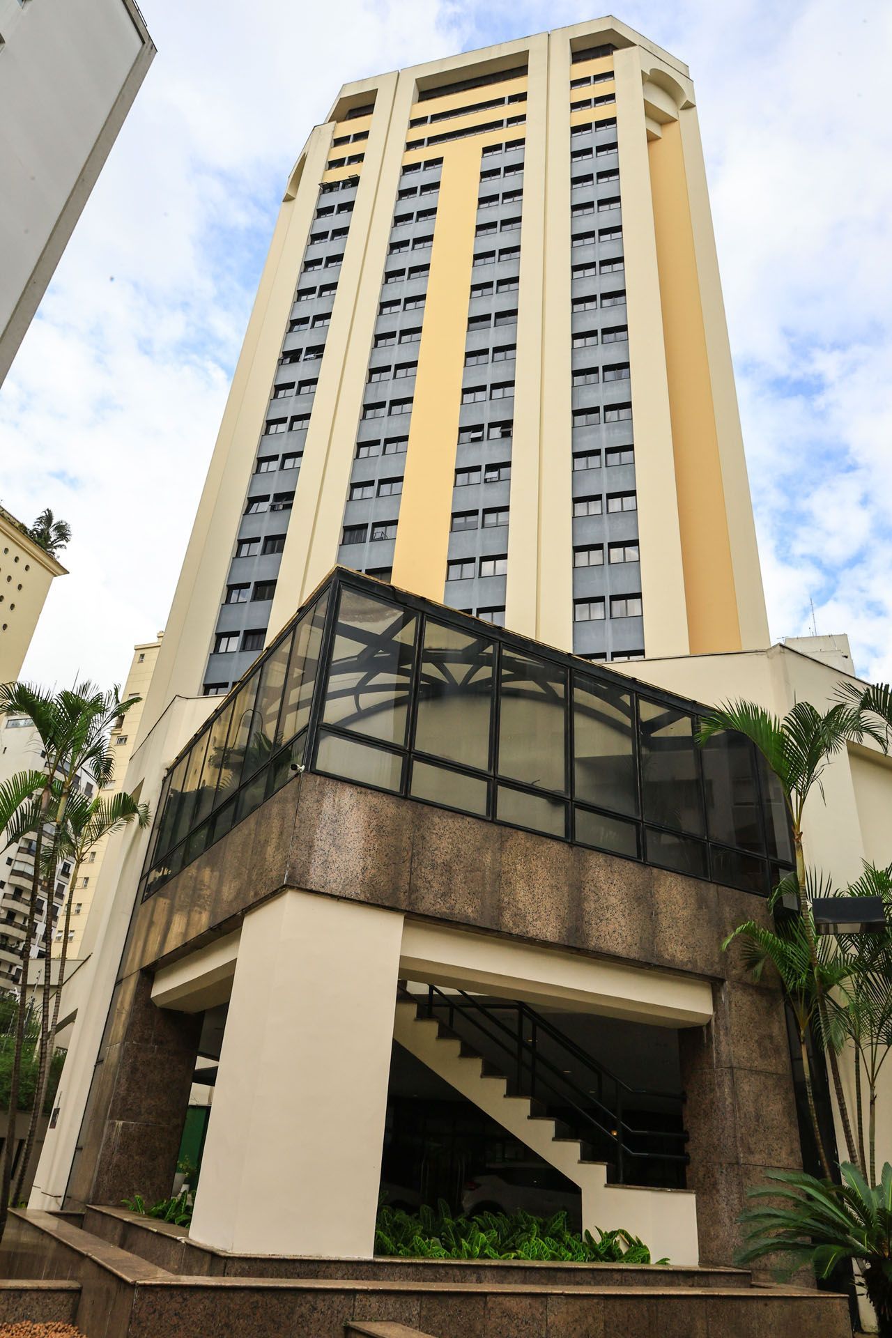 Prédio alto bege com entrada e escadaria externa cobertas por vidro.