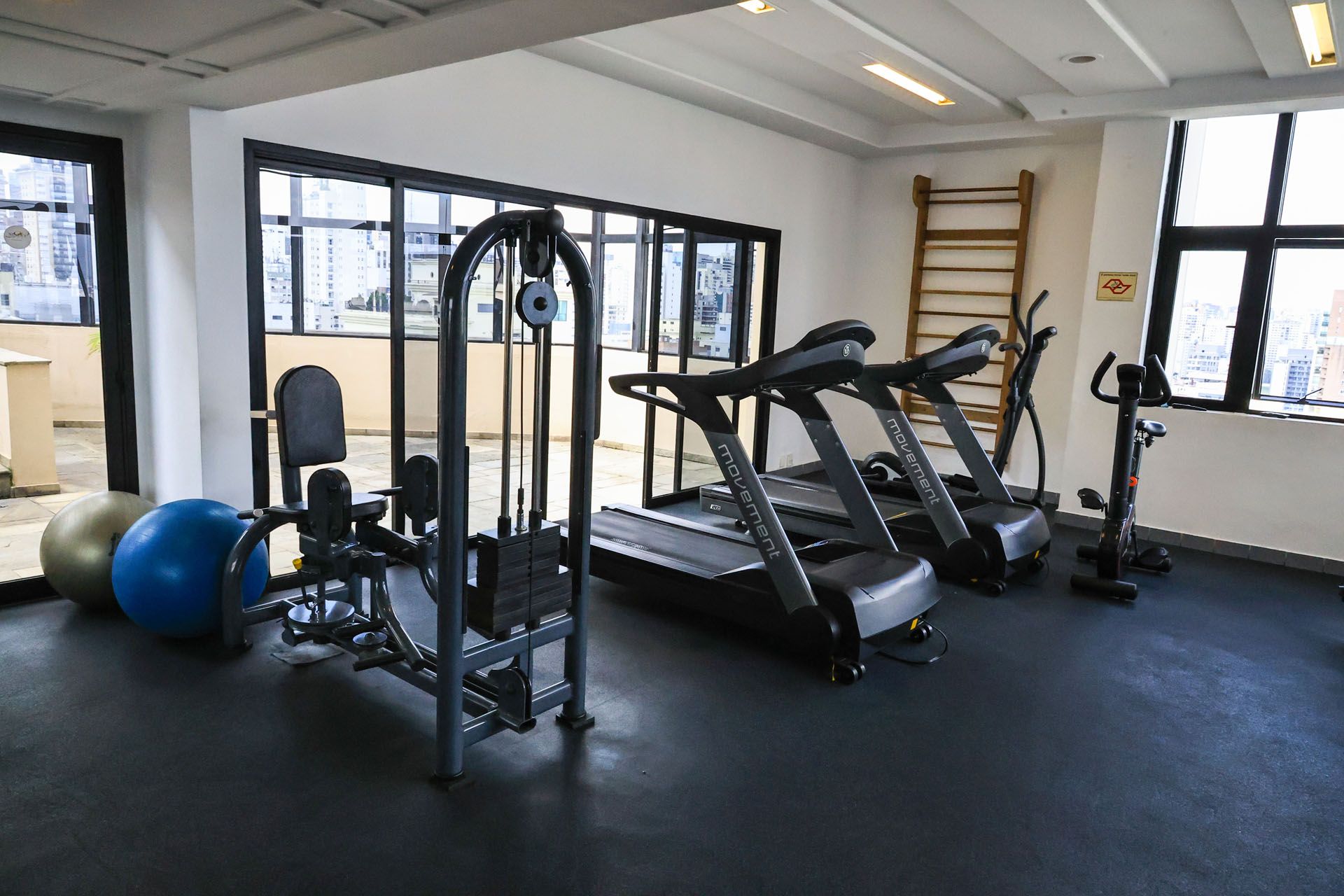 Sala de ginástica vazia com esteiras, aparelhos de musculação, bolas de exercício e barras de parede.