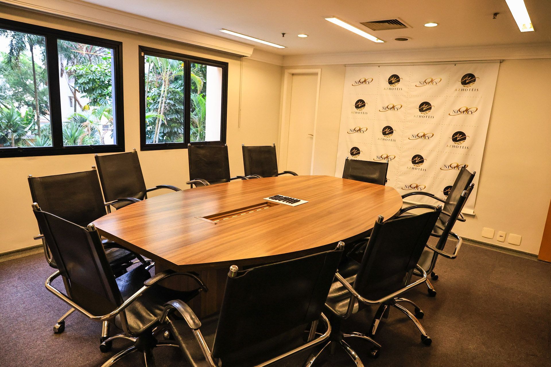 Sala de conferências com mesa oval, laptops, garrafas de água e cadeiras de escritório pretas ao redor.
