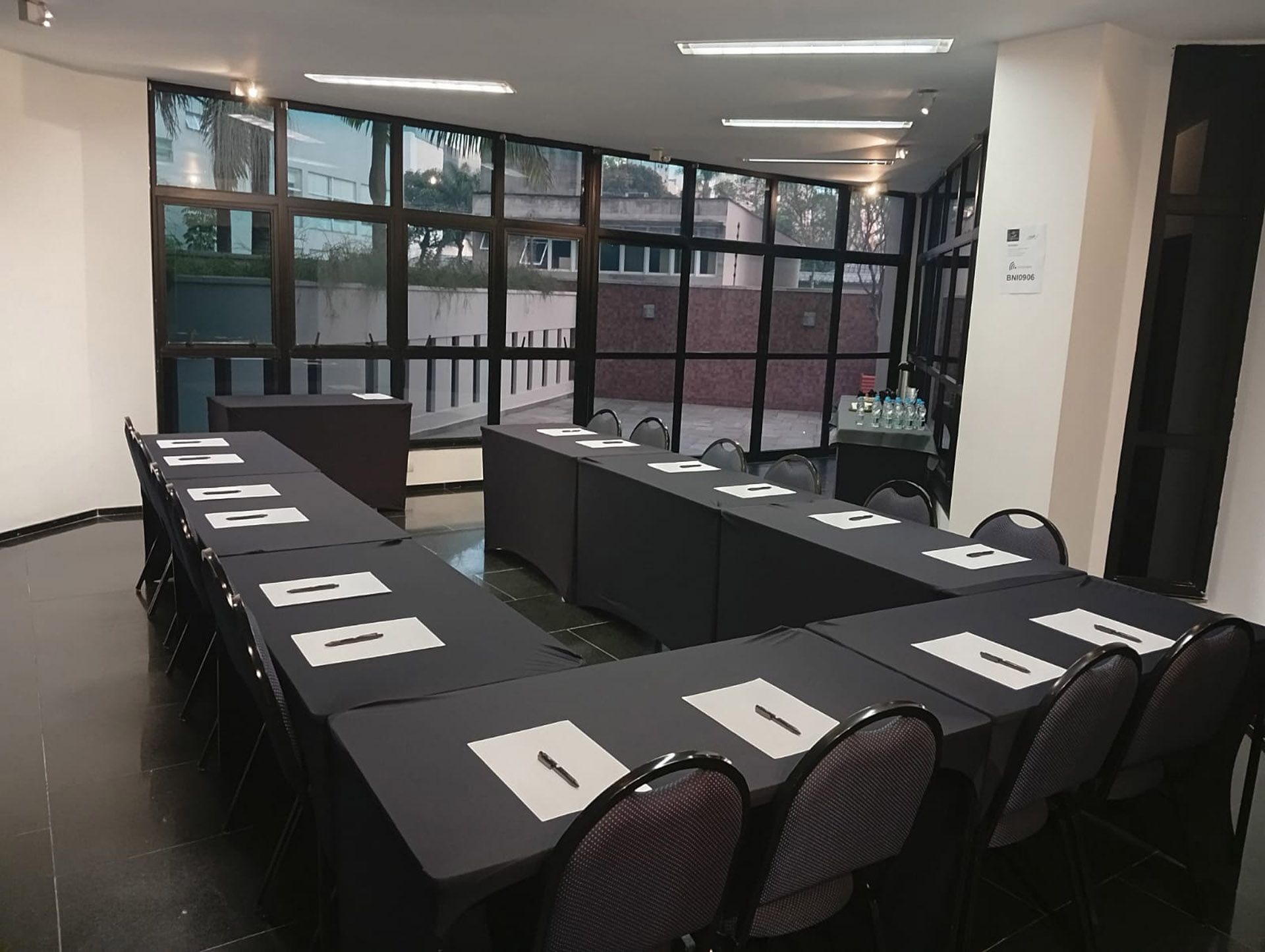 Sala de conferências com mesa oval, laptops, garrafas de água e cadeiras de escritório pretas ao redor.