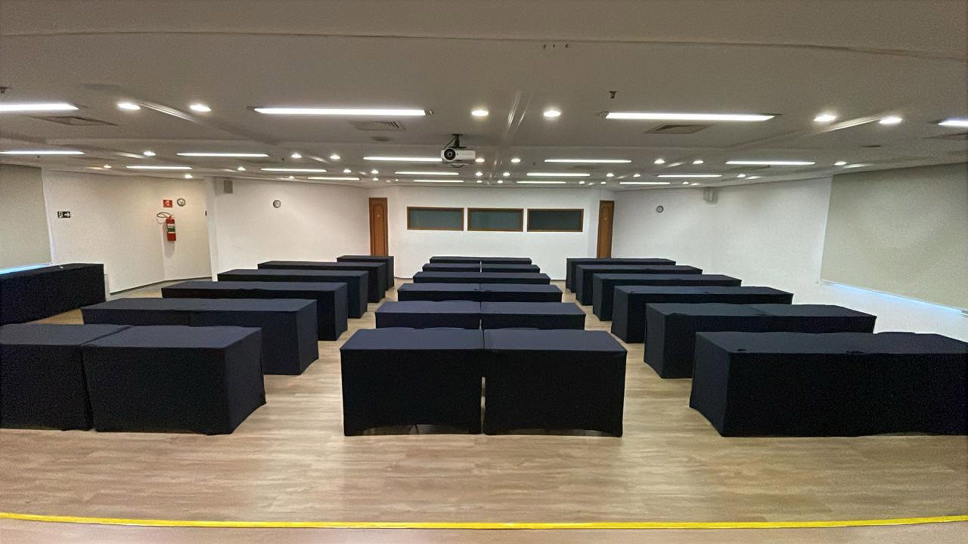 Sala de conferências vazia com fileiras de cadeiras azuis voltadas para um palco e uma tela.