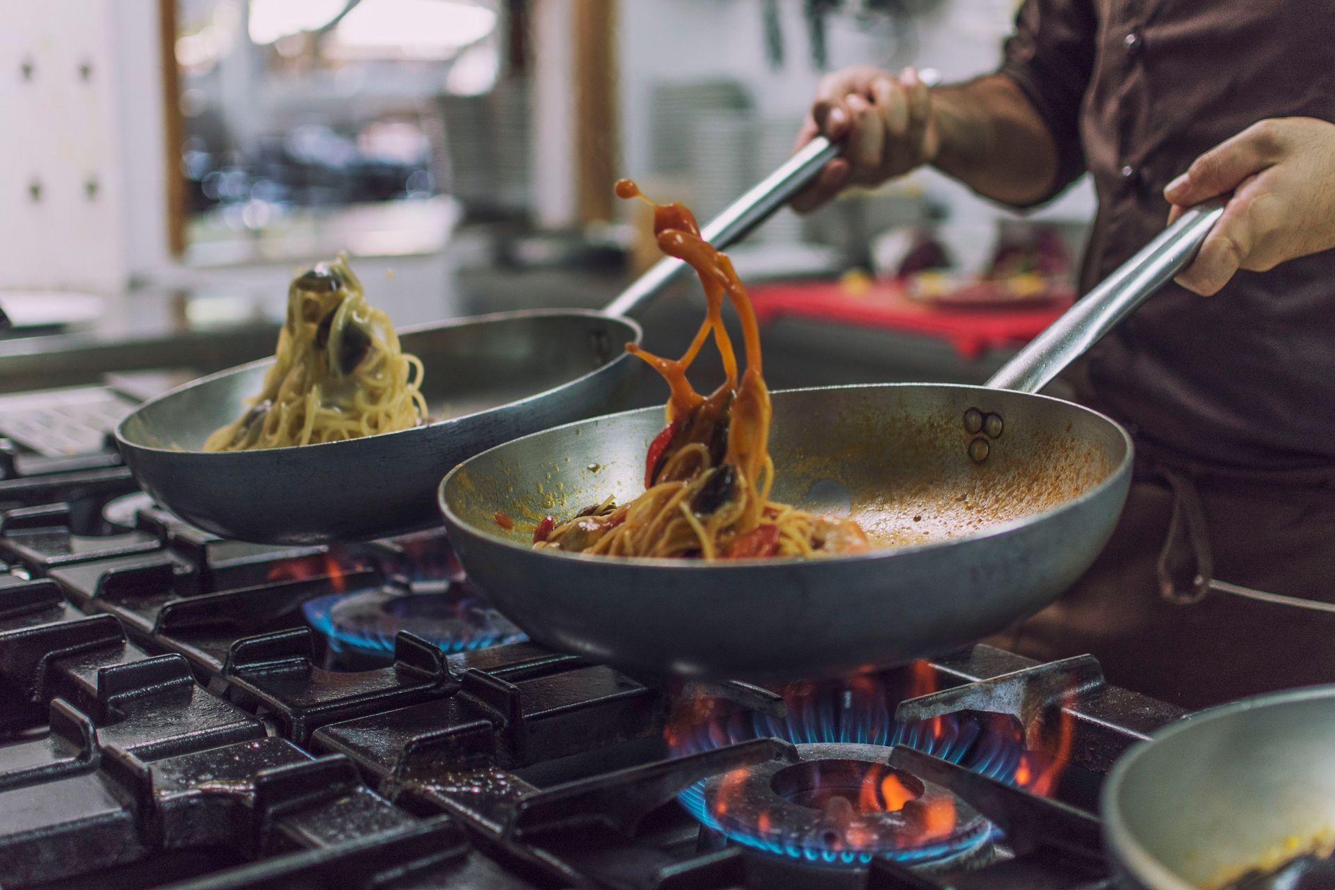 Chef che lancia la pasta in una padella su un fornello a gas. Il sugo vola. Ambiente cucina.