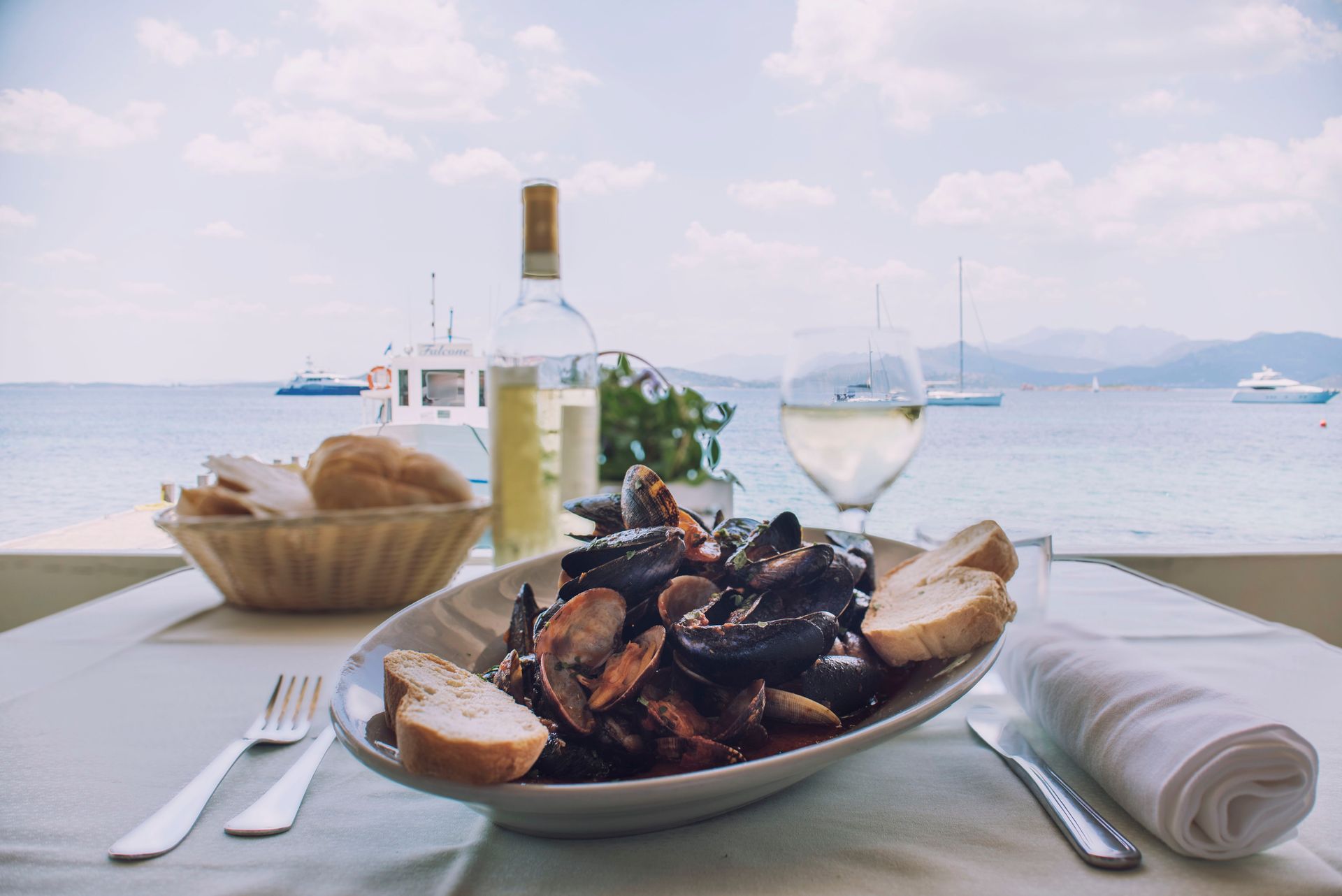 Piatto di frutti di mare con pane, vino e vista sul mare da un tavolo all'aperto del ristorante.
