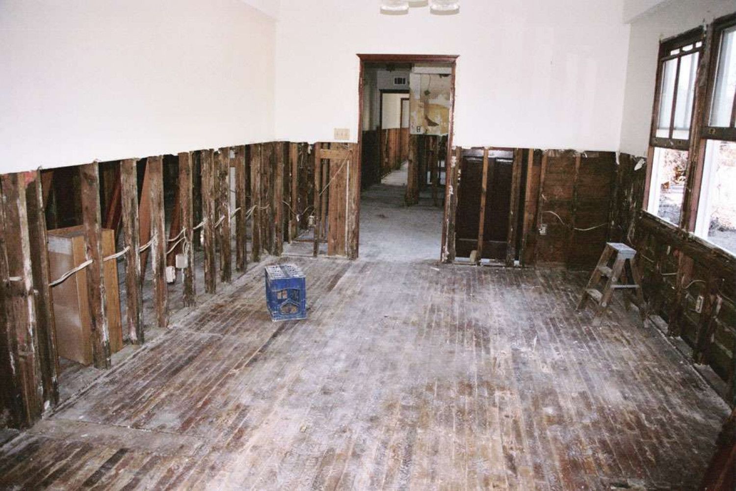 Room gutted, walls stripped to studs. Floorboards exposed. Doorways and windows visible.