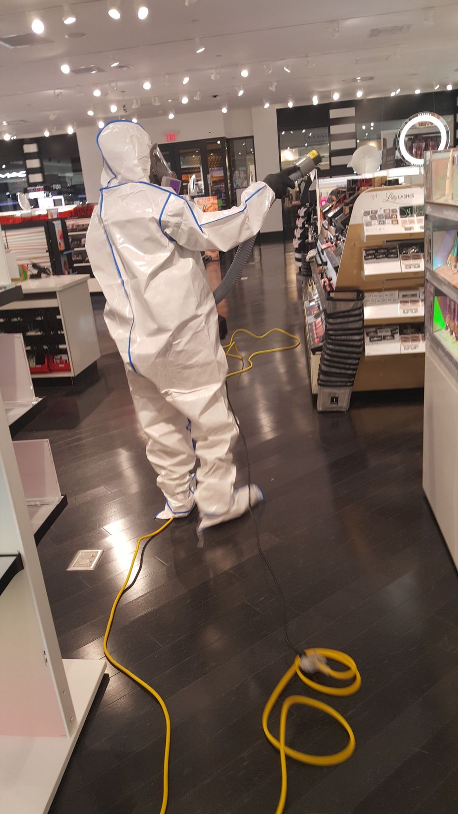 Person in hazmat suit disinfecting a store with a yellow cord attached.