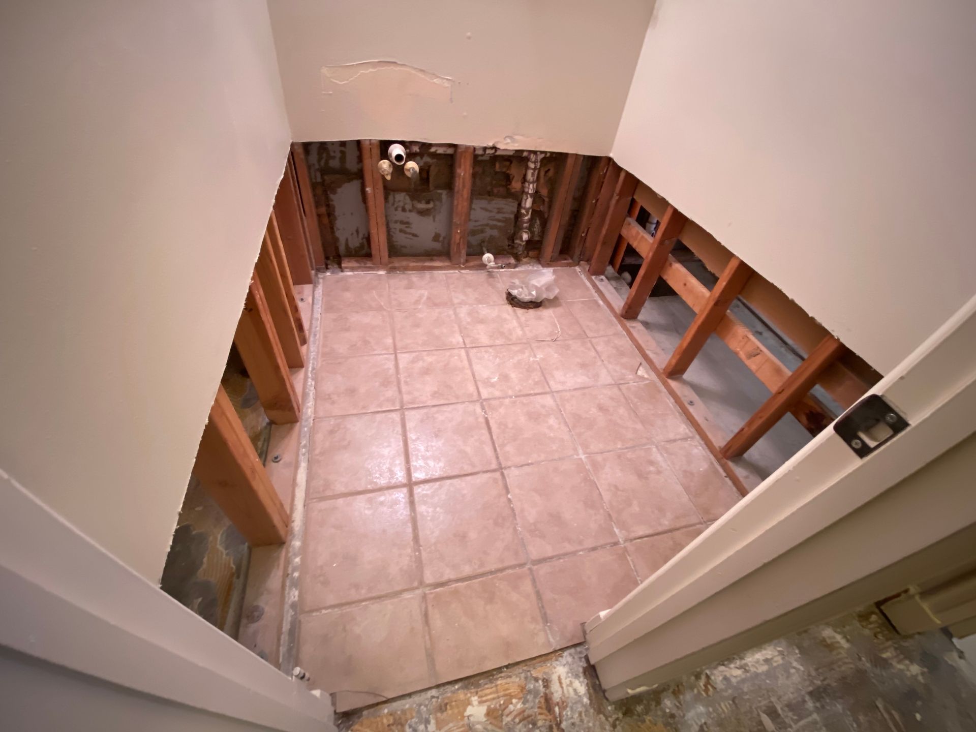 Bathroom renovation in progress; exposed studs, tile floor, hole in ceiling, beige walls.