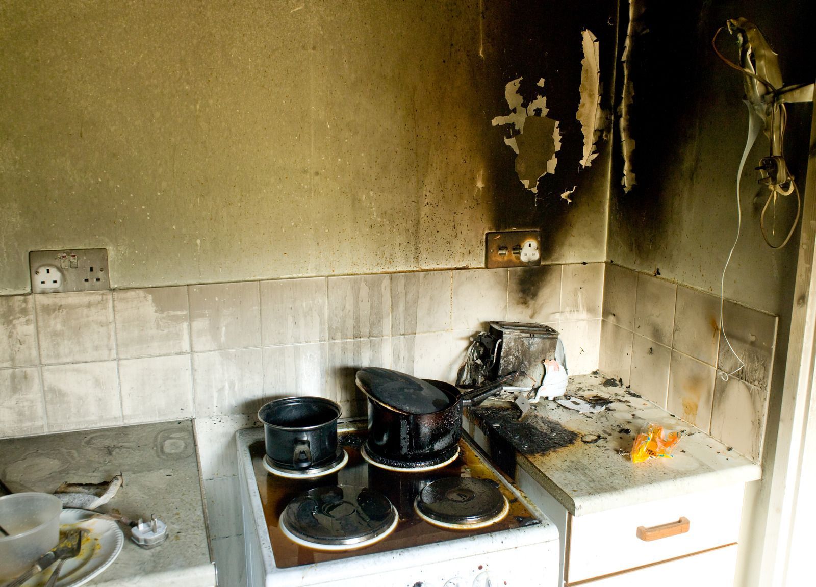 Kitchen interior heavily damaged by fire; burnt stove, cabinets, and walls are visible.
