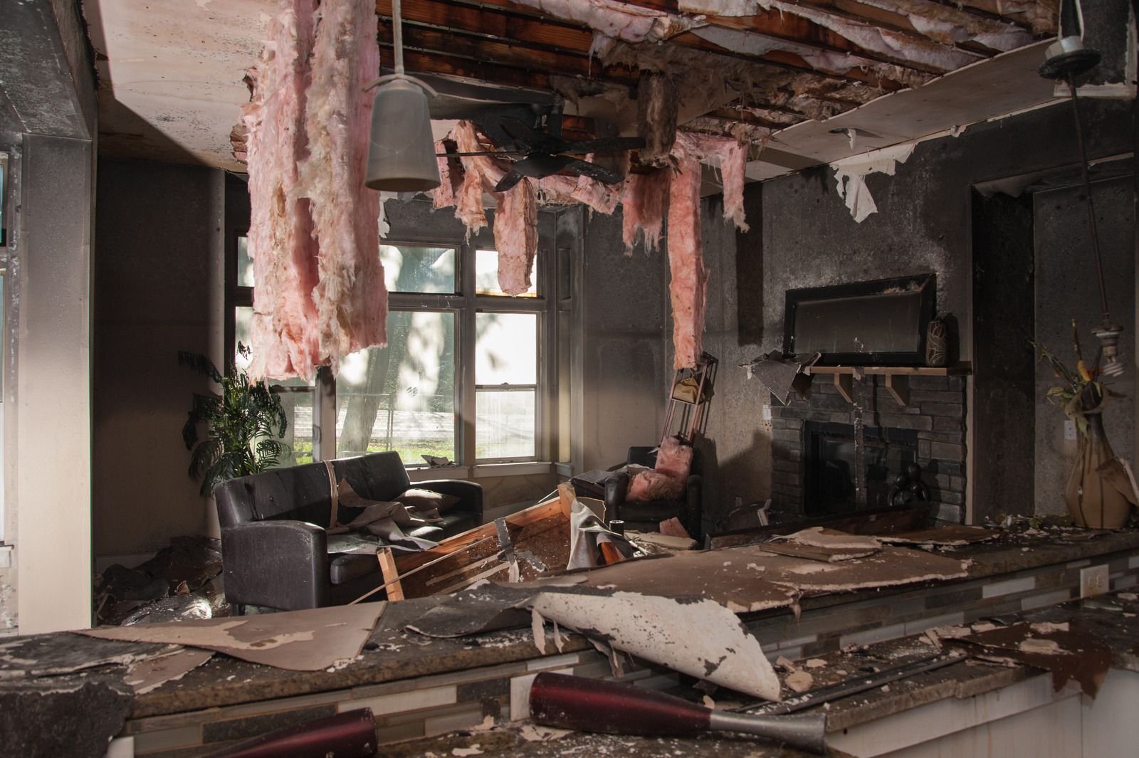 Interior of a damaged room after a fire; exposed ceiling, debris, furniture, and a fireplace.
