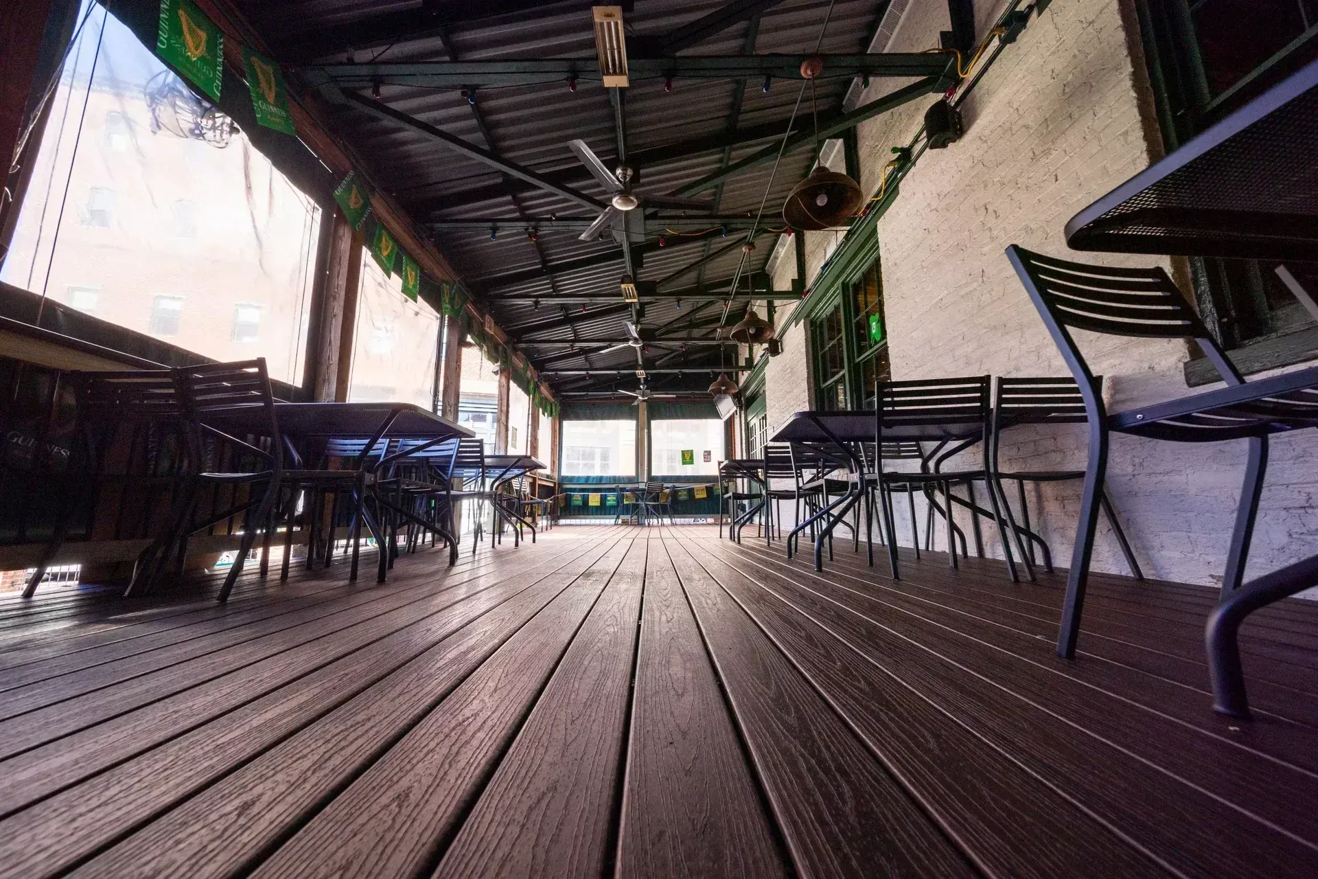 A low-angle view of a wooden restaurant deck featuring several tables and chairs under a covered roof with ceiling fans.