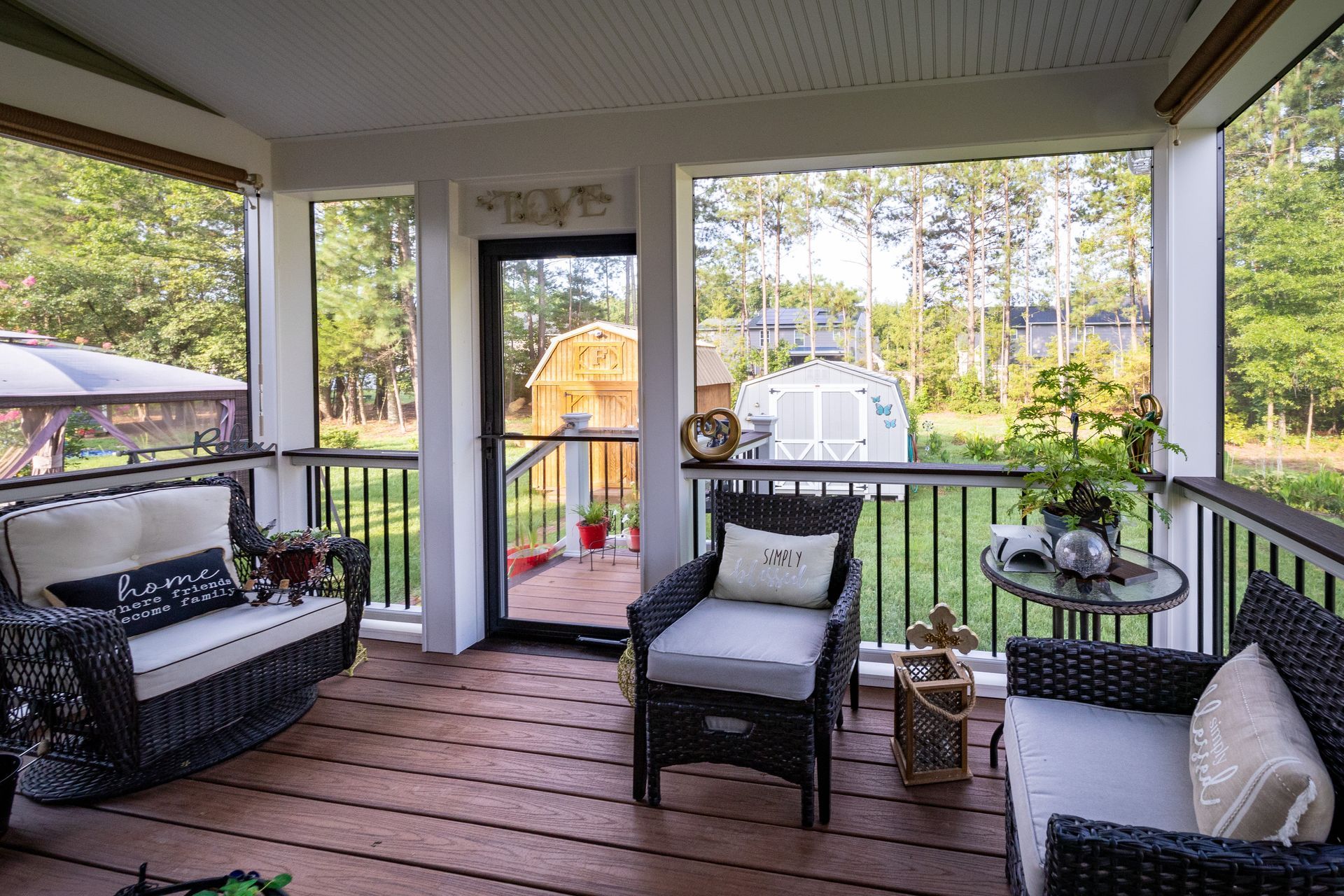 Two white wicker rocking chairs with red cushions on a wooden porch, featuring red shutters and a black wall lantern.