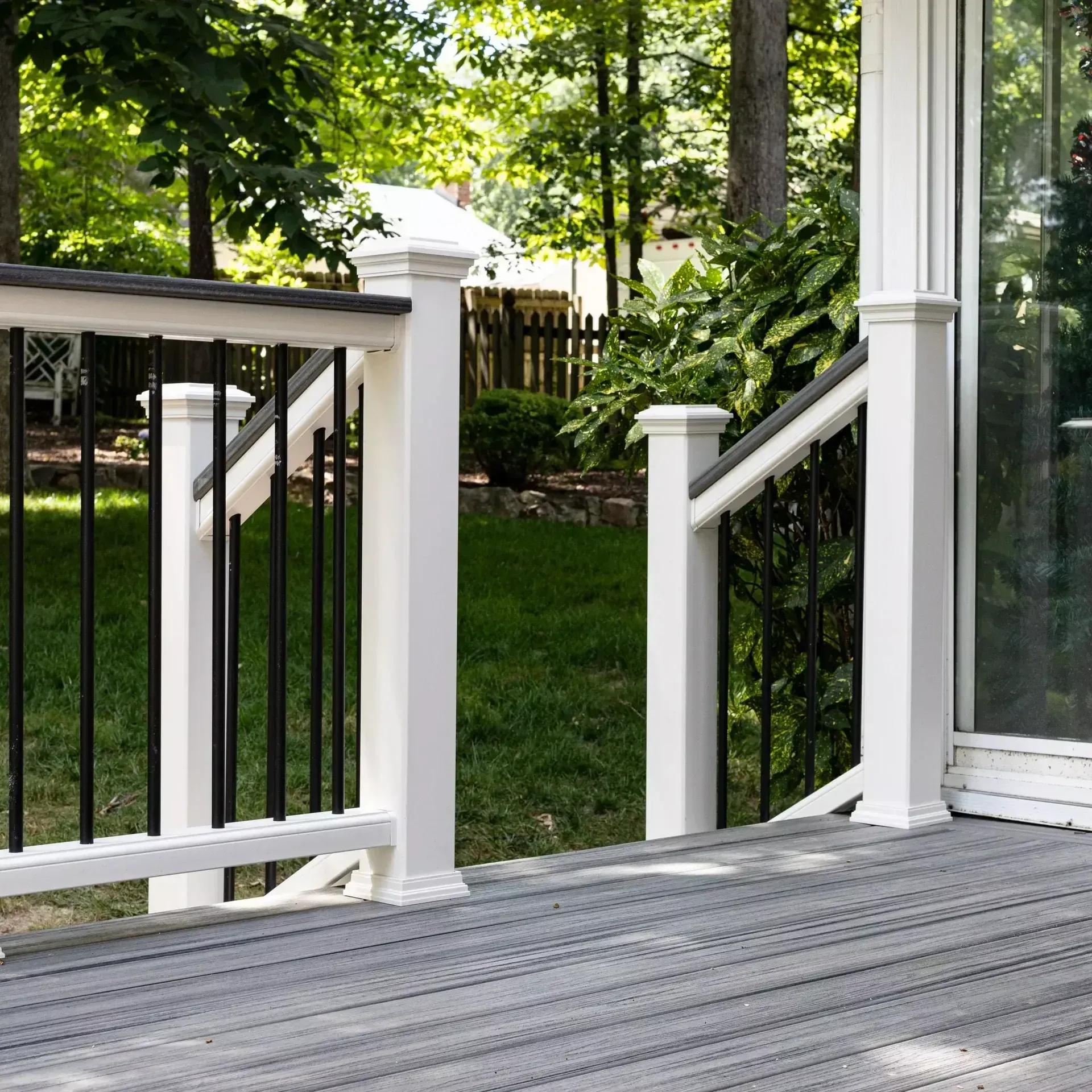 A gray composite deck featuring a white railing with black metal balusters, overlooking a lush green backyard.