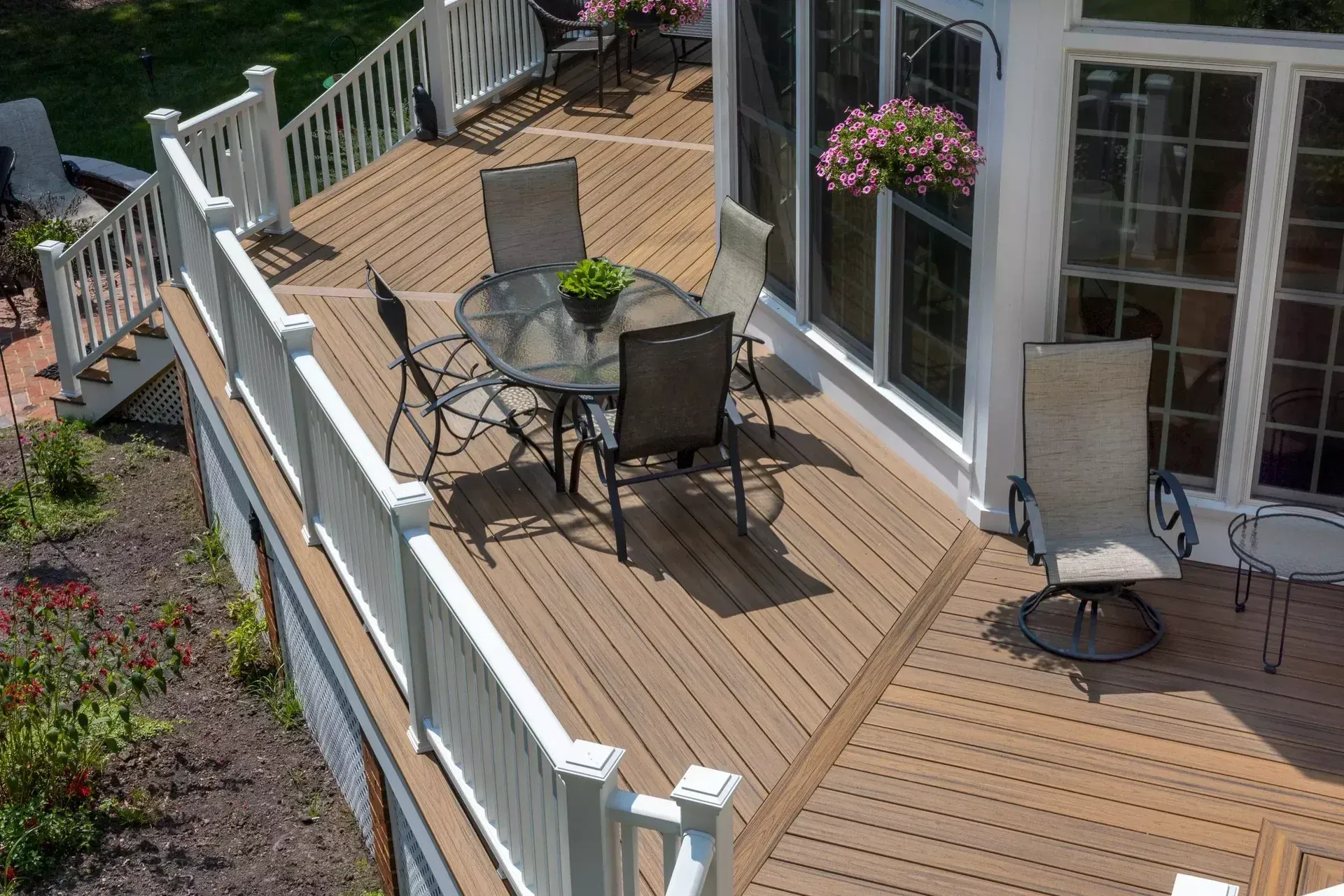 An elevated wood-look deck with white railings, a glass-topped table set, and outdoor chairs outside a home.