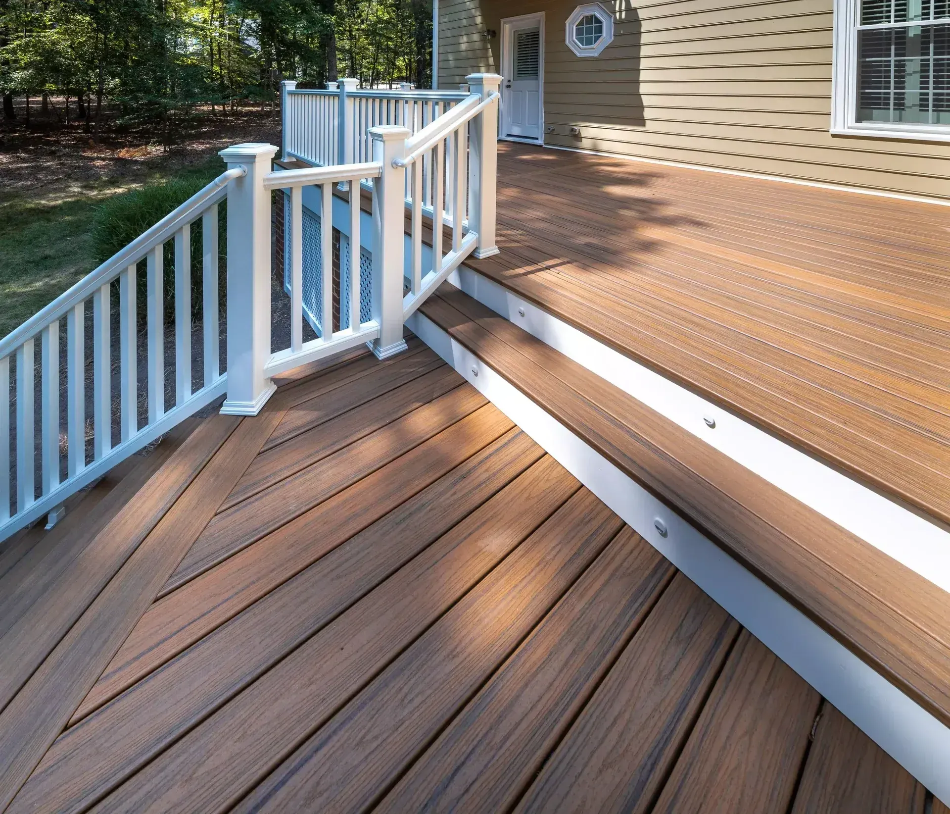A wood-plank deck features stairs, white railings, and integrated step lighting against a house with tan siding.