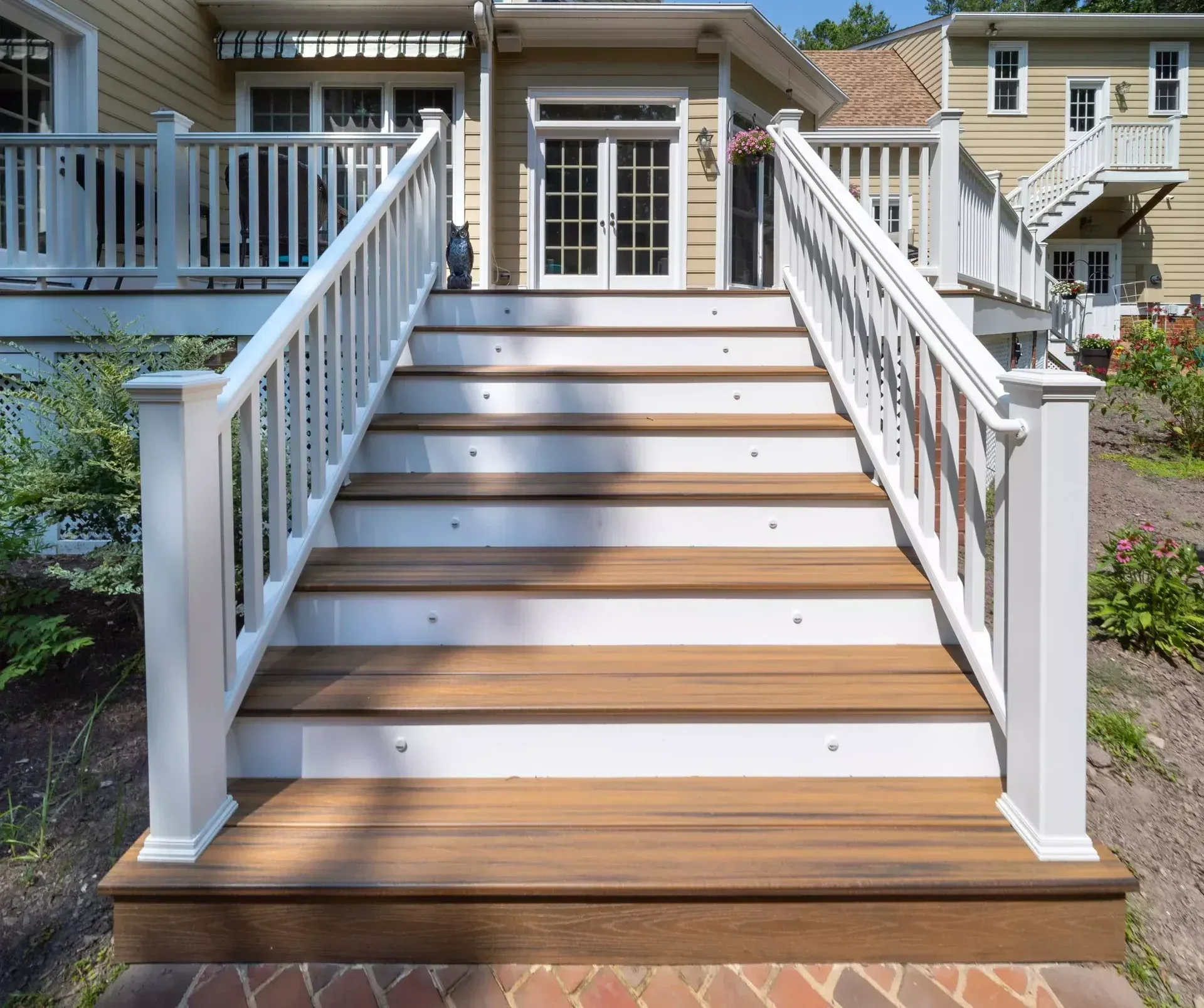 A set of brown wooden stairs with white railings leading up to the back door of a yellow house.