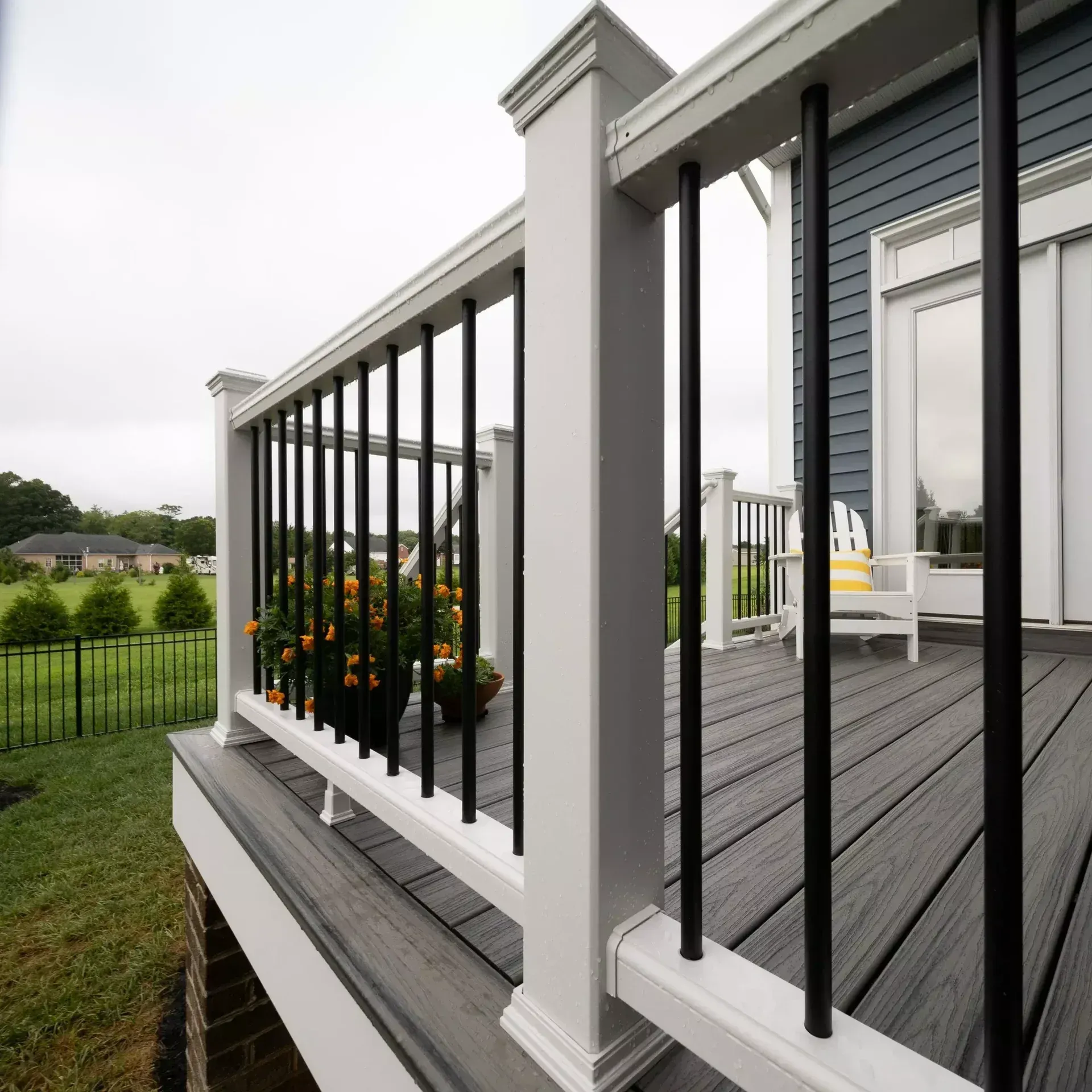 A raised backyard deck with gray composite flooring, white posts, and black metal railings, overlooking a green lawn.