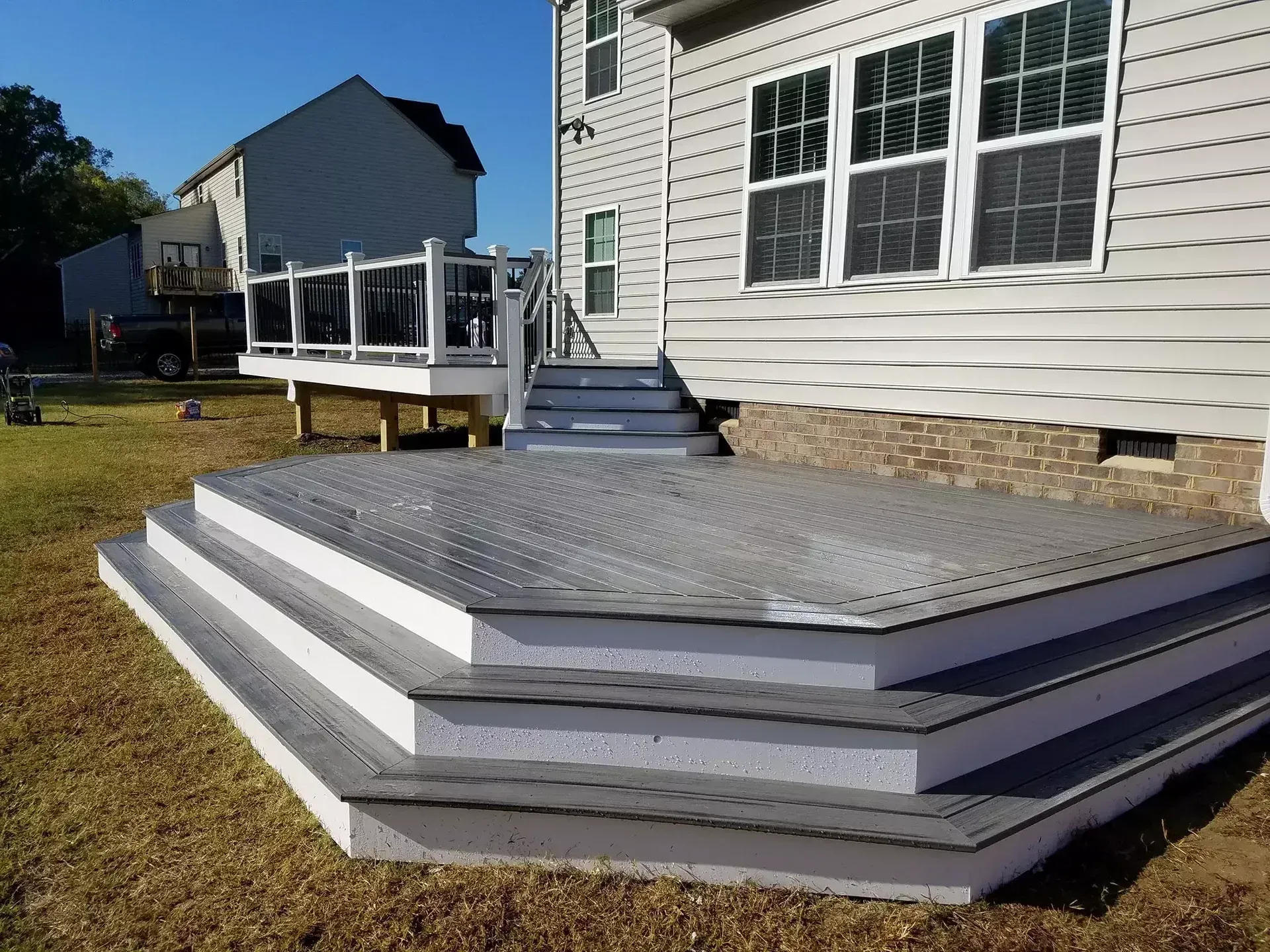 A multi-level gray composite deck with white risers and railings sits against the back of a light-sided residential home.