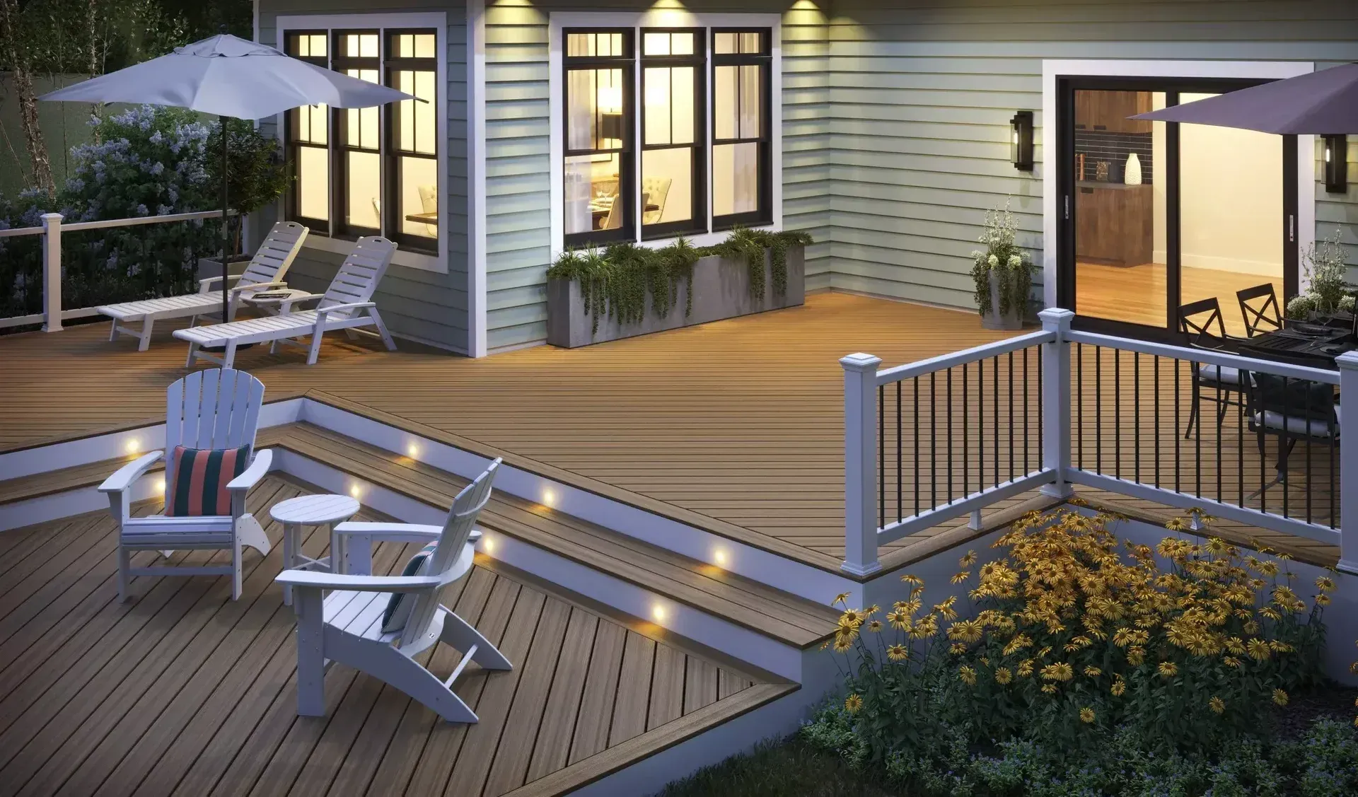 A multi-level outdoor wooden deck with lounge chairs, a patio table, and ambient lighting, attached to a house at dusk.