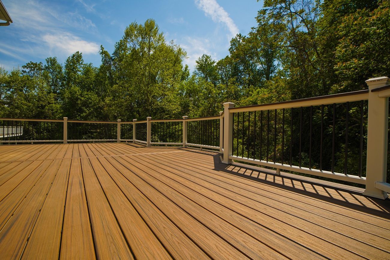 A dark wood deck with planks laid at an angle, leading to a modern home with glass doors and outdoor patio chairs.
