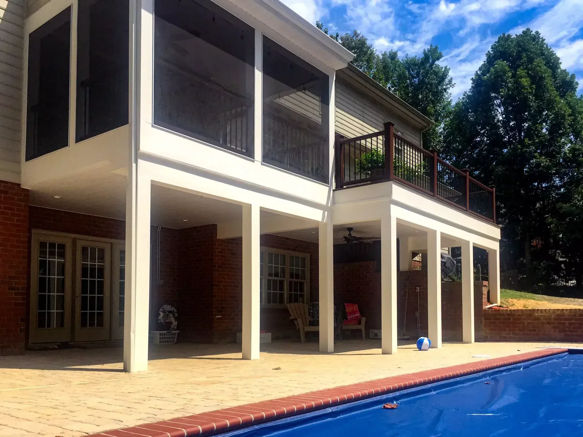A two-story home with a screened-in porch above a patio area and an adjacent deck overlooking a blue swimming pool.