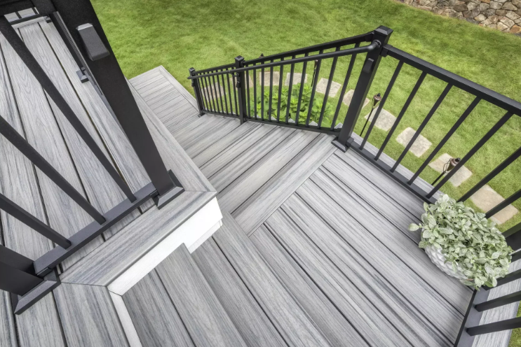 Gray composite deck stairs and landing with black metal railings, overlooking a green lawn with stone pavers.