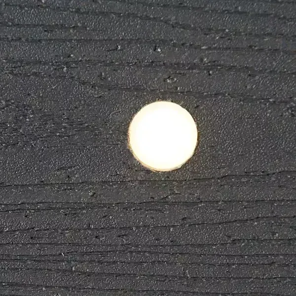 A small, bright, circular light glowing against a dark, textured surface with horizontal grain lines.