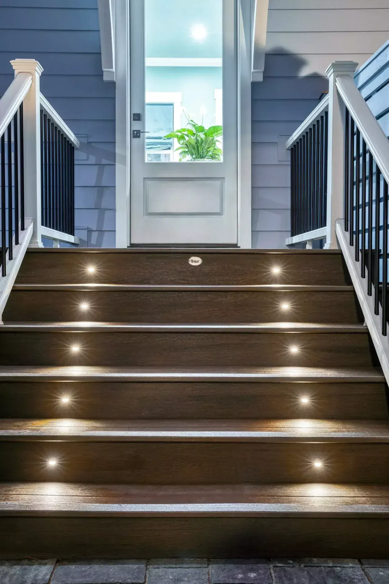A set of wooden stairs with built-in LED lights leading up to a white door at night.