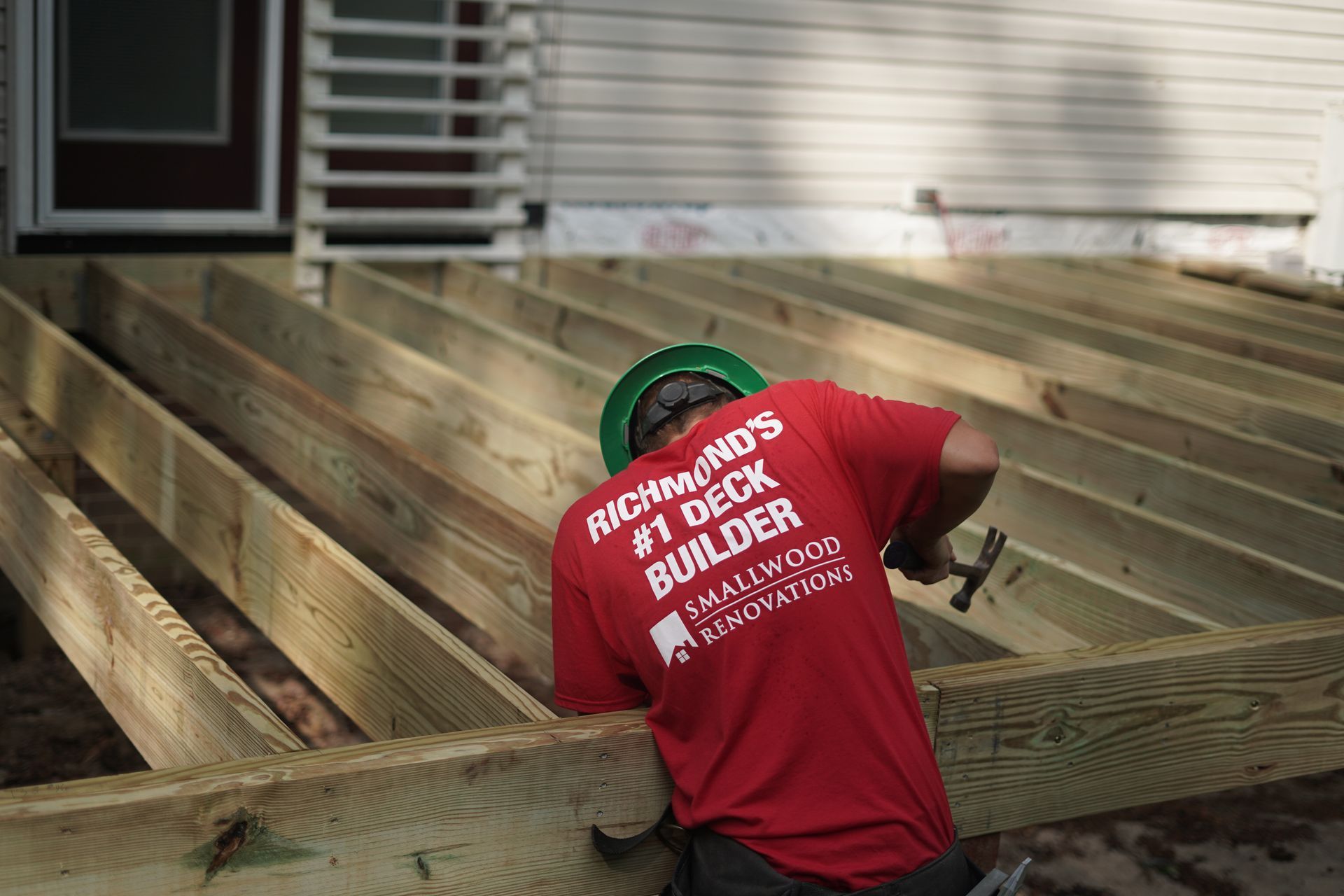 Worker in red shirt assembling a wooden deck beside a house.