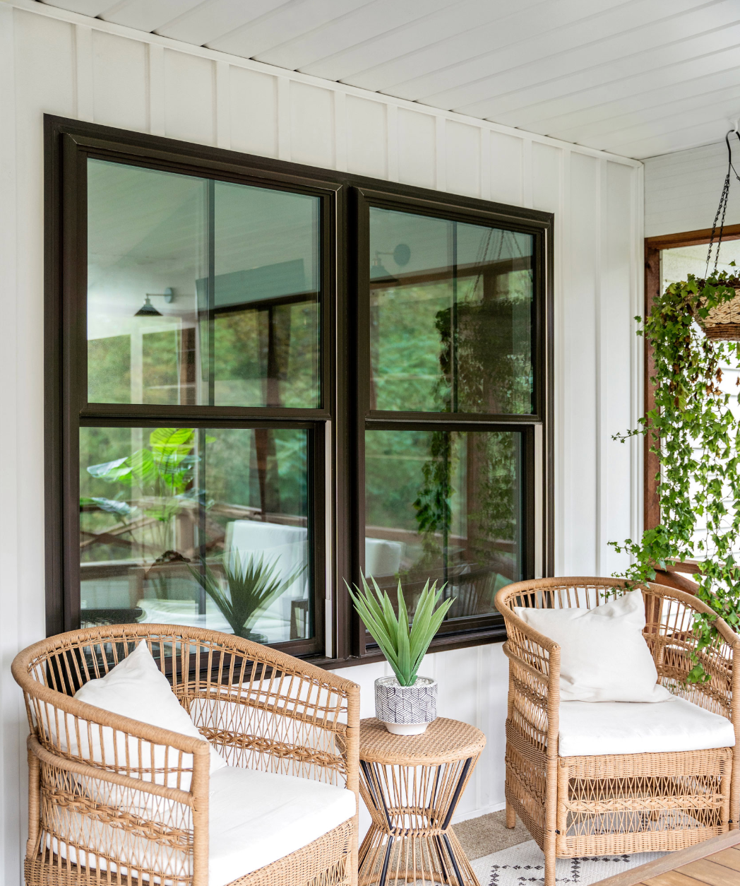 Two wooden rocking chairs on a covered porch with dark siding, ceiling fans, and potted plants.
