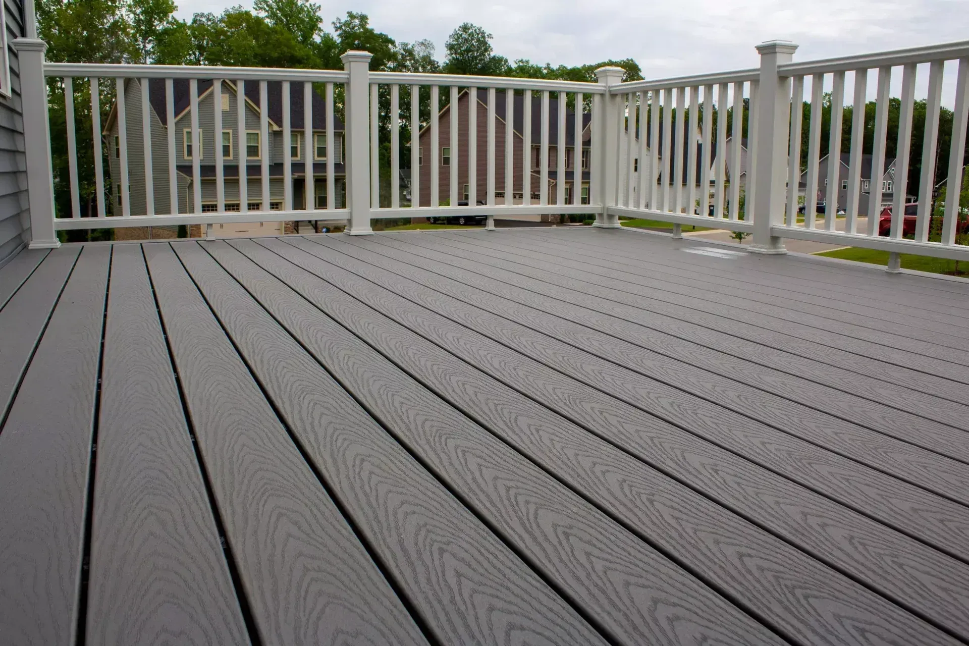 A gray composite deck featuring wood grain texture with a white railing overlooking a suburban backyard.