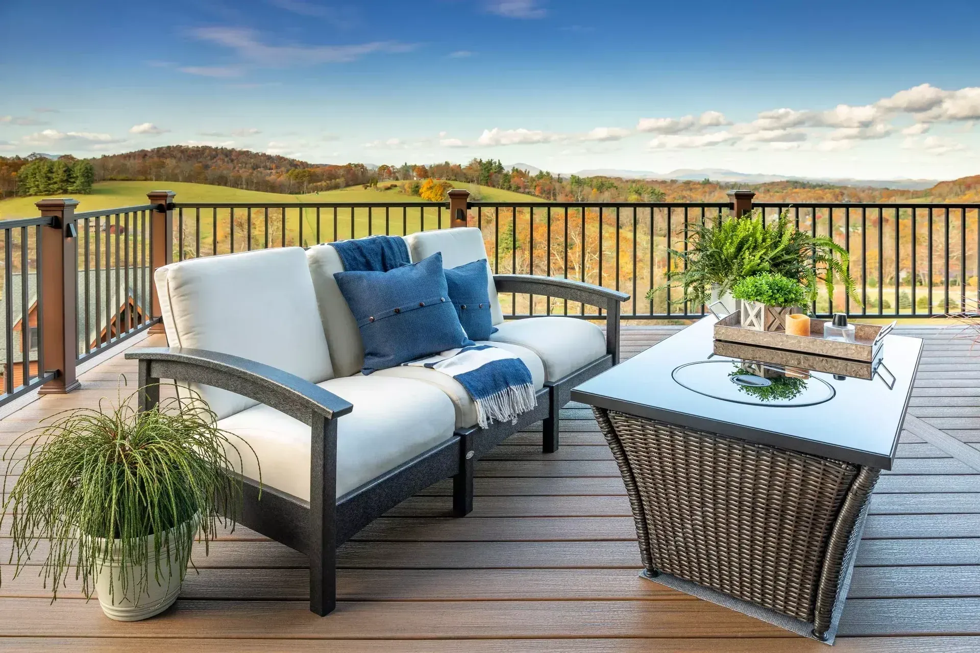 Outdoor patio furniture with a cushioned sofa and glass-topped table on a wooden deck overlooking a rural landscape.