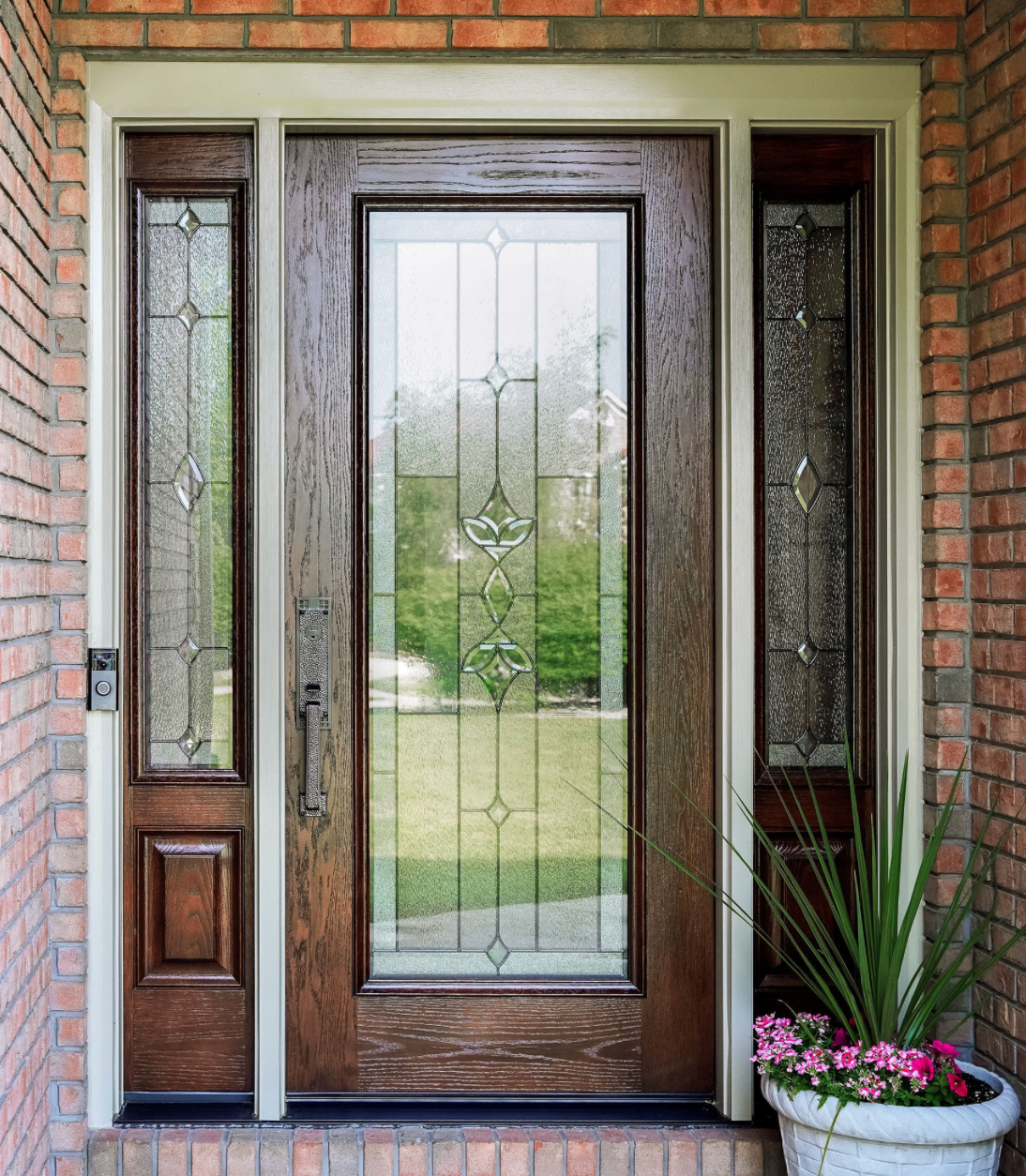 A dark wooden front door with a single window pane, framed by white siding, stone pillars, and two black exterior lanterns.