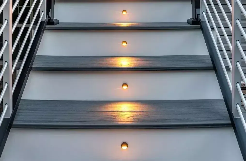 Modern staircase with dark gray treads, white risers, metal railings, and small circular warm lights on each riser.