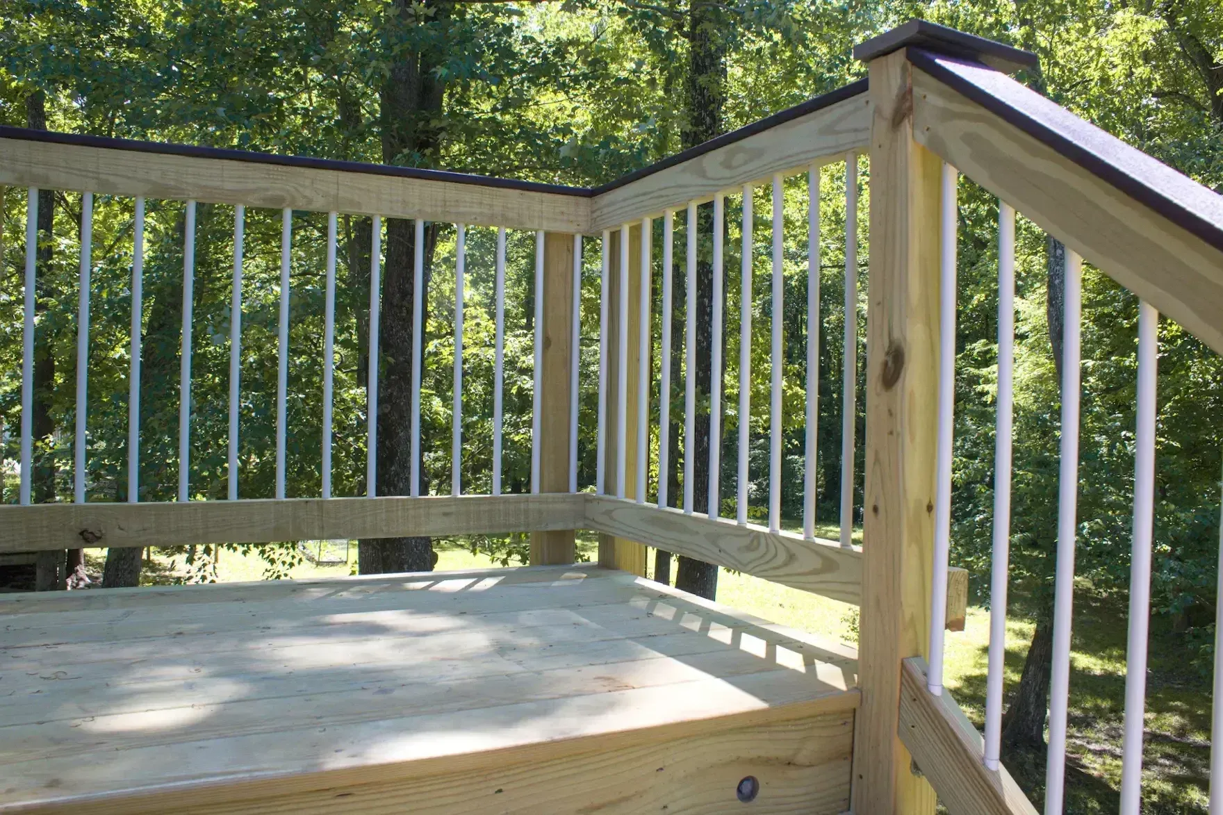 A wooden deck with a railing featuring white vertical balusters, overlooking a forested area.