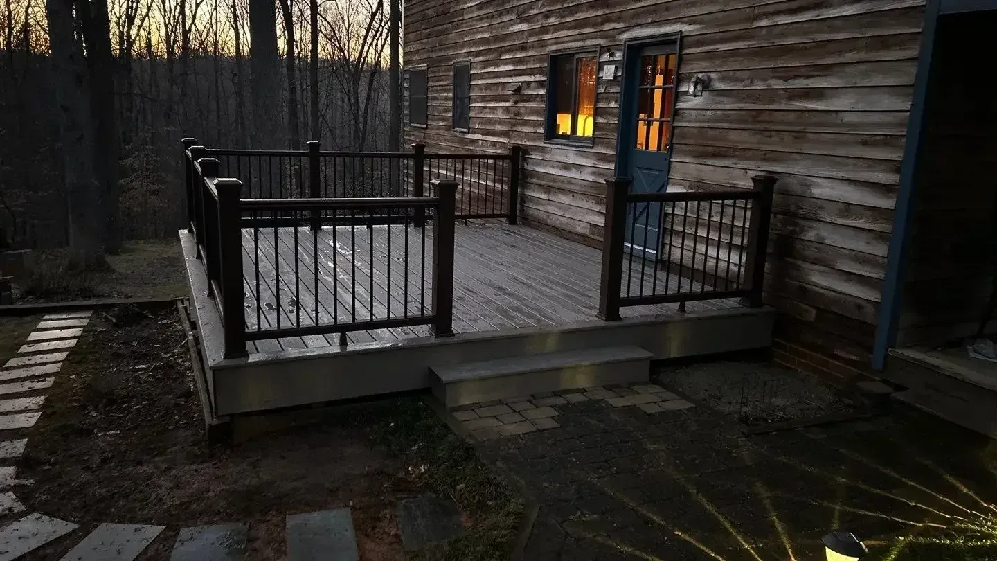 A wooden deck with a black railing attached to the side of a rustic log home at dusk.