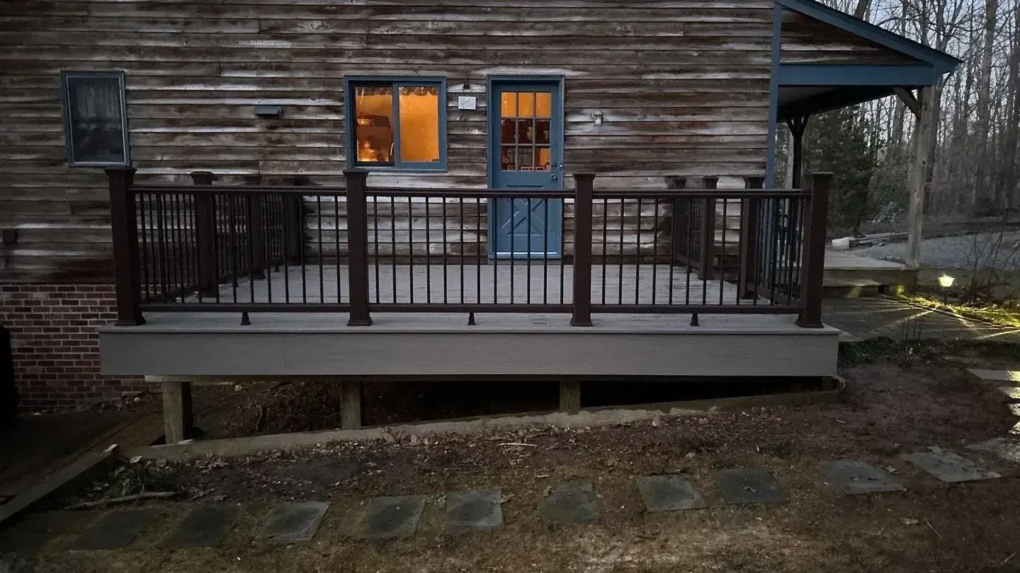A newly built composite deck with dark railings attached to the side of a rustic log cabin home.