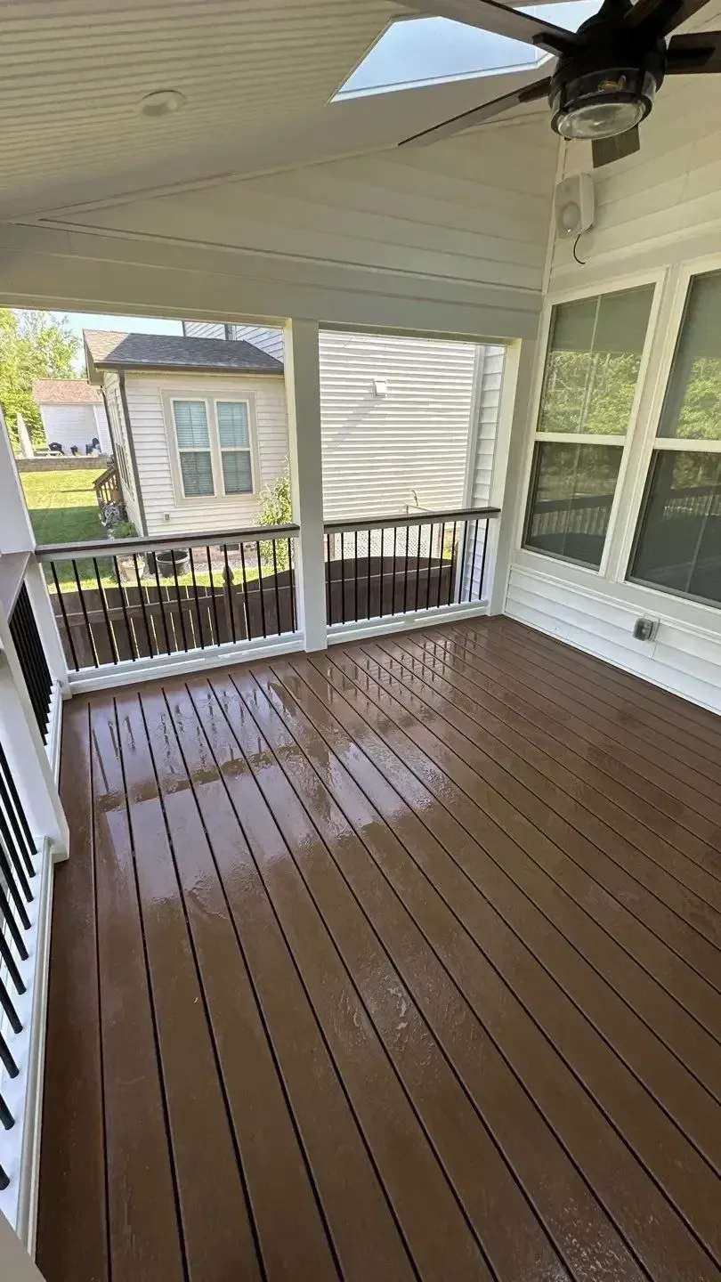A covered wooden deck with a ceiling fan, white railing, and exterior views of a neighboring house.