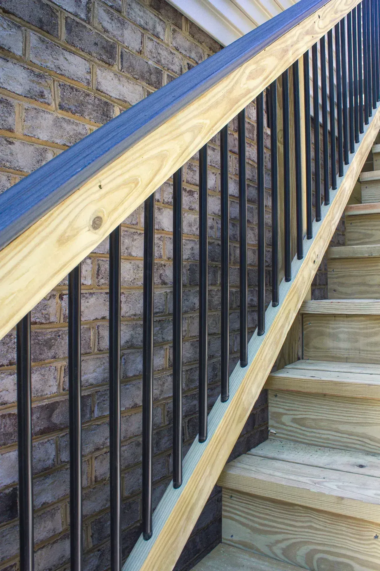 A staircase with wooden steps and a handrail featuring a natural wood top rail and black vertical metal balusters.