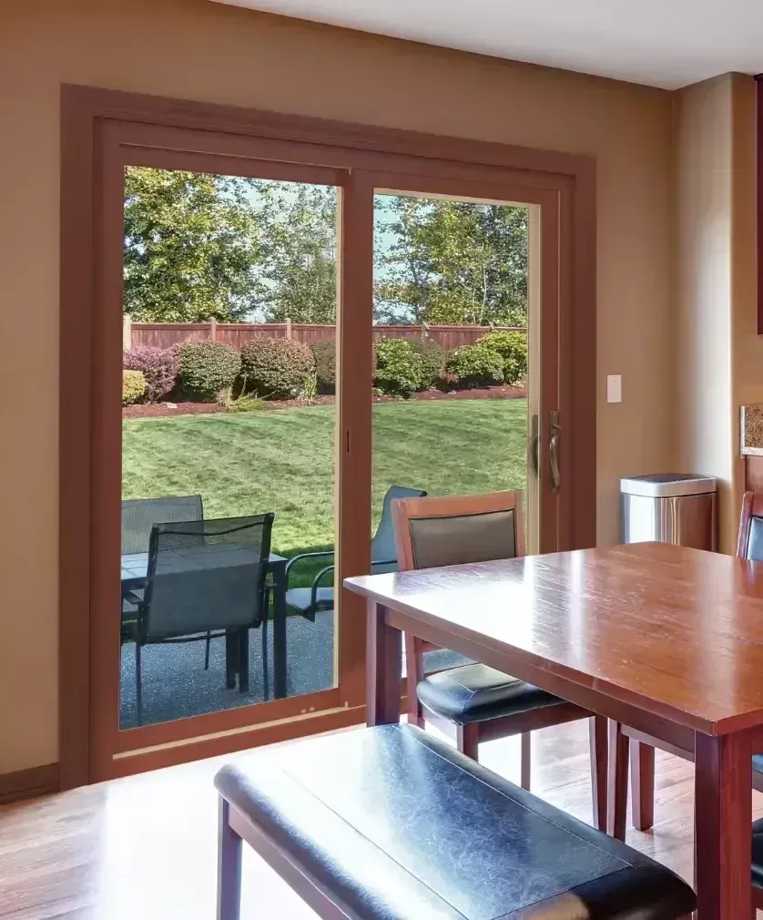 A brown-framed sliding glass door opens to a backyard patio with a dining set, viewed from inside a dining room.
