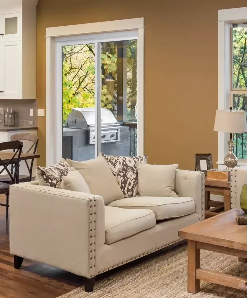 A beige tufted loveseat with patterned pillows in a living room next to a sliding glass door and wooden coffee table.