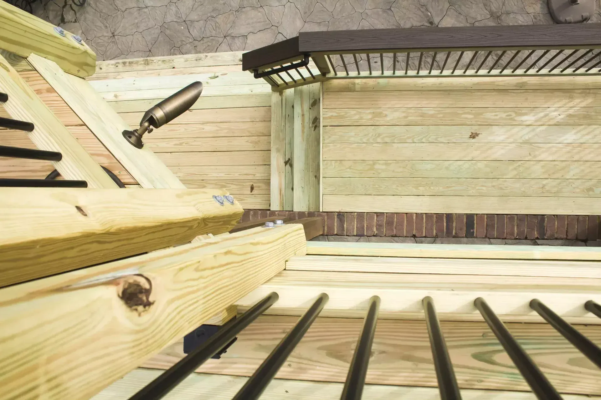 A high-angle view looking down at a wooden deck with dark metal railings and a small, angled porch light.