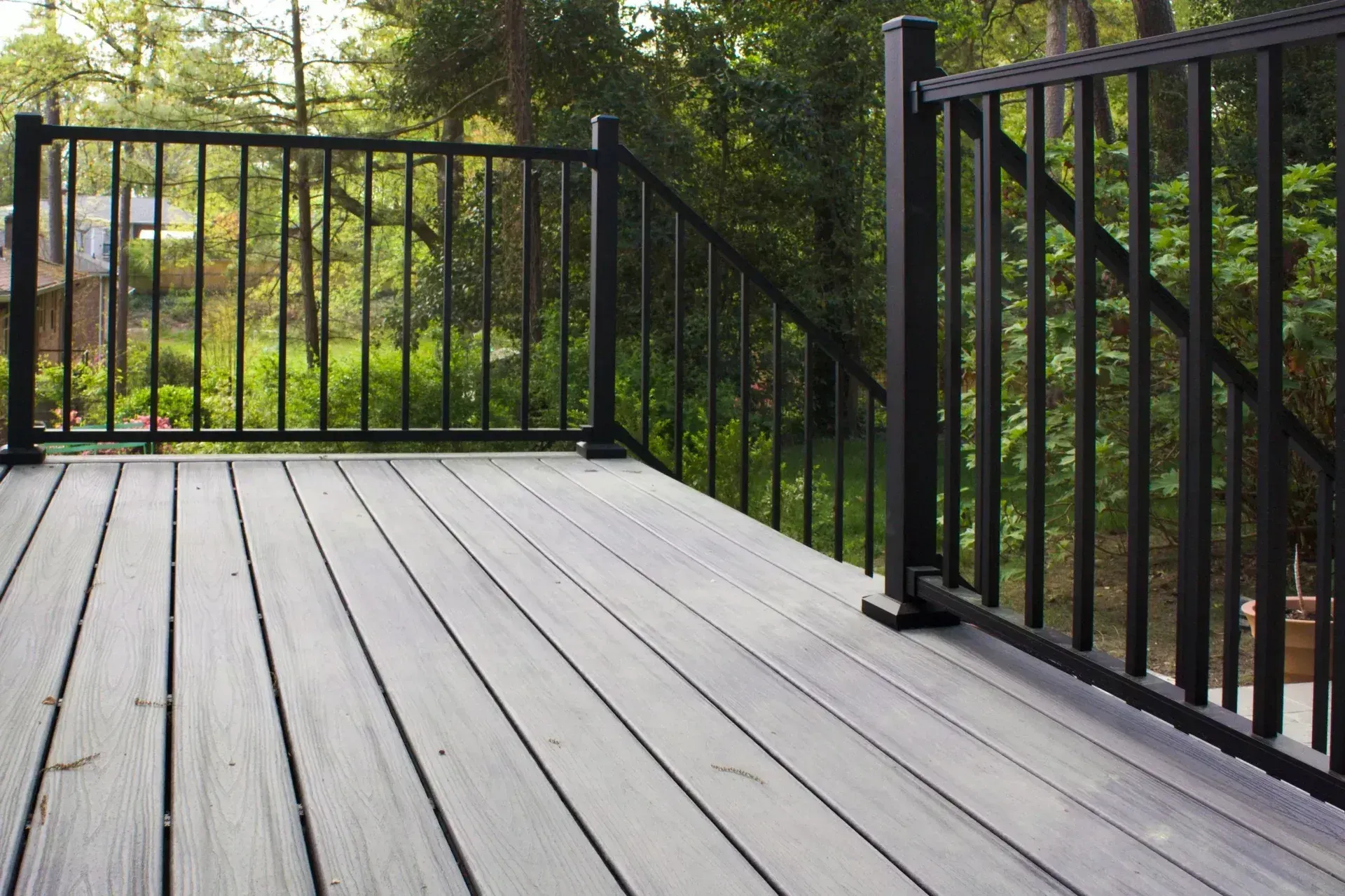A gray composite deck featuring black metal railings and stairs overlooking a green, tree-filled backyard.