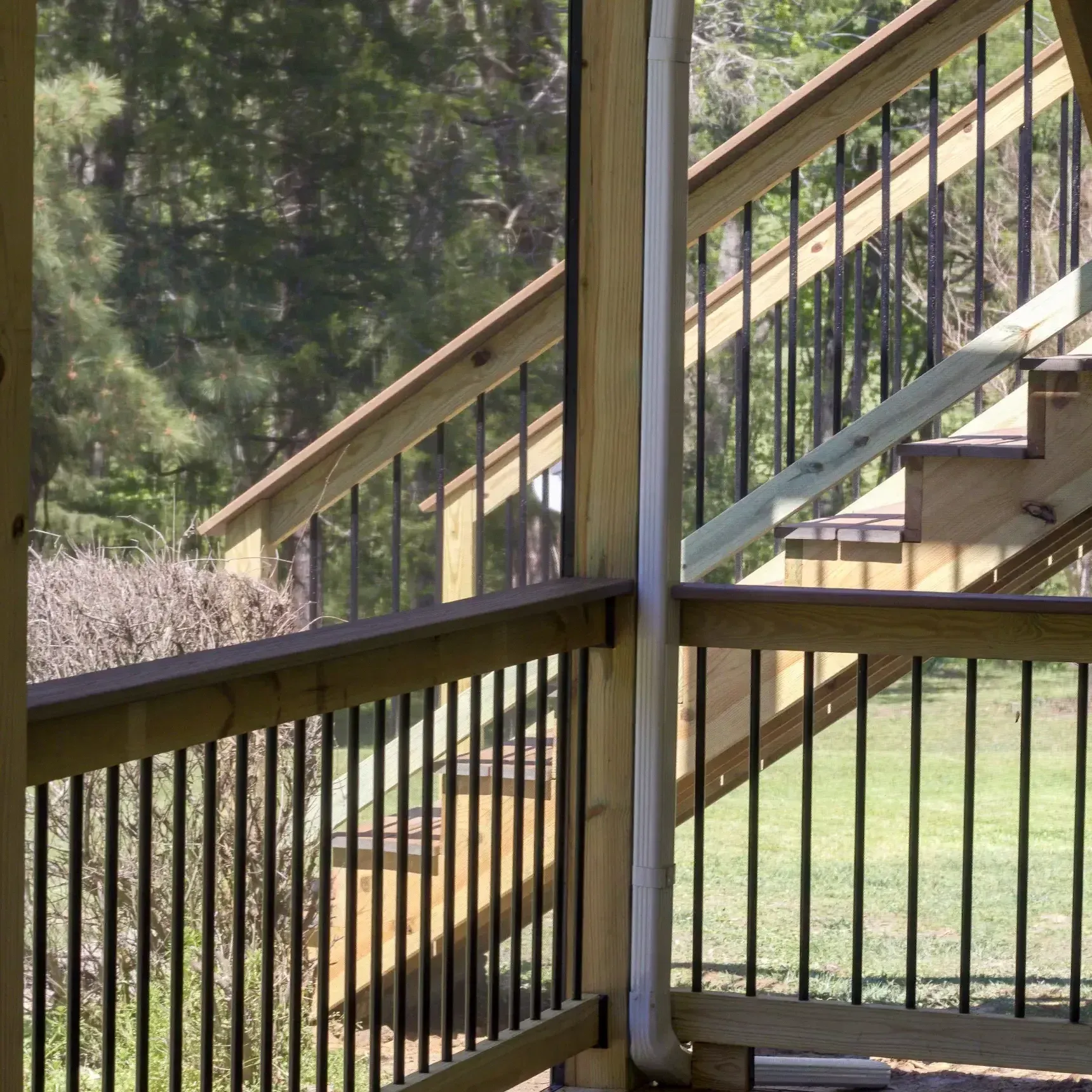 Wooden deck with black metal railing and stairs leading down to a lawn, viewed through a screened porch.