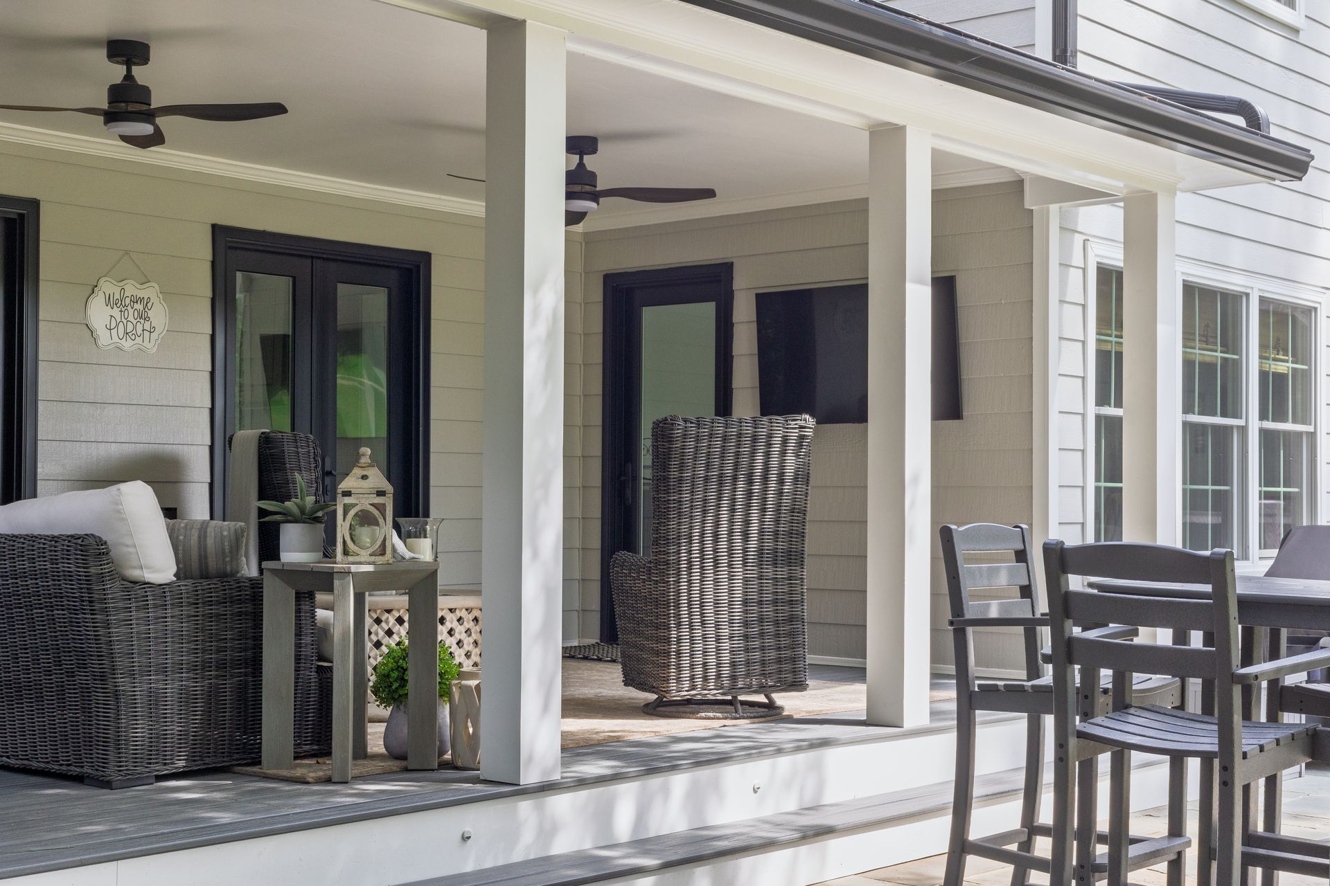 Two white rocking chairs on a covered wooden porch with white railings and house siding with dark shutters.
