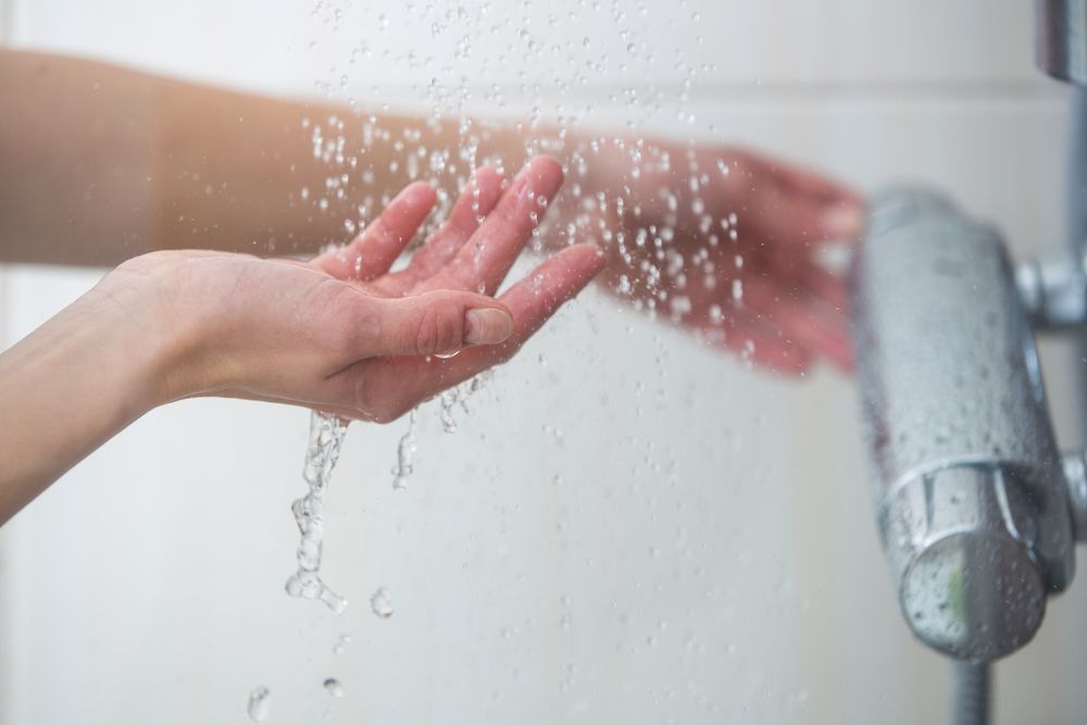 Woman taking a shower at home - female hands tryimg the temperature of water in shower