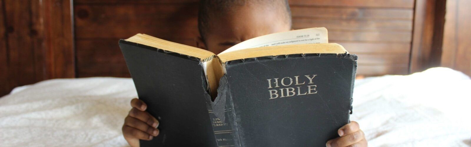 a young boy is reading a holy bible on a bed .