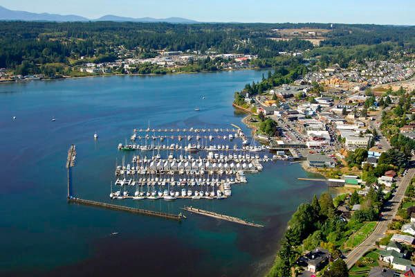 Aerial view of a marina with boats, a coastal town, and calm blue water beside a green shoreline