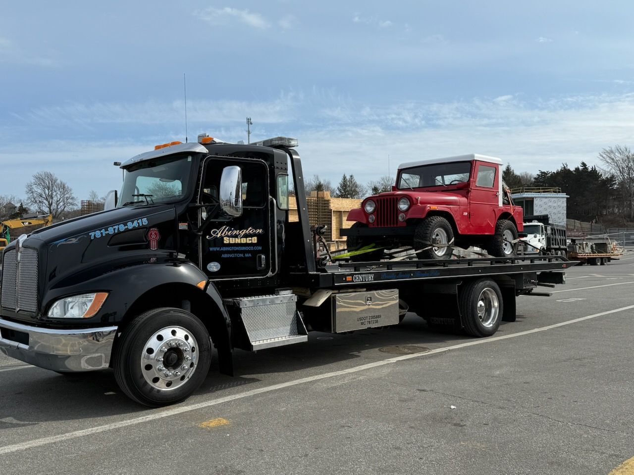 A tow truck is carrying a red jeep on the back of it.