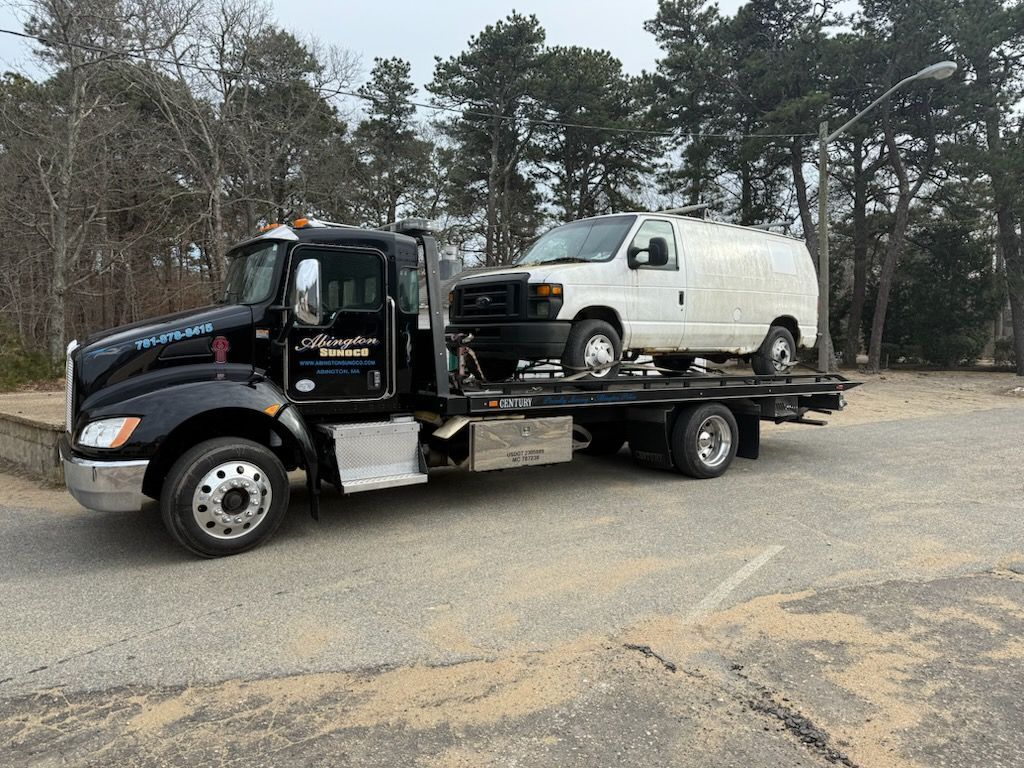 A black tow truck is towing a white van in a parking lot.