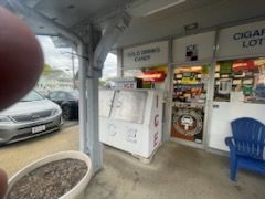 A person is taking a picture of a store with a car parked in front of it.